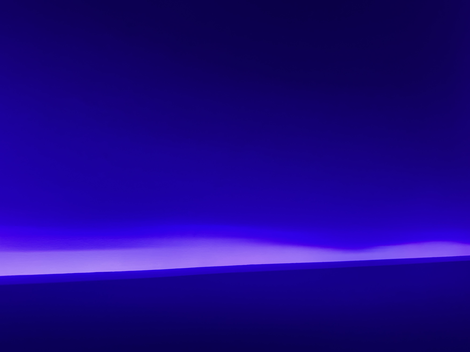The image is an abstract close-up of a surface bathed in blue and pink light, with a distinct bright pink vertical band on the left side. The lighting suggests an artificial environment, potentially an interior space. There are no identifiable landmarks or features that would place this image specifically in Burgas, Bulgaria. The scene is devoid of people or discernible objects, focusing solely on the interplay of light and color on a textured surface.