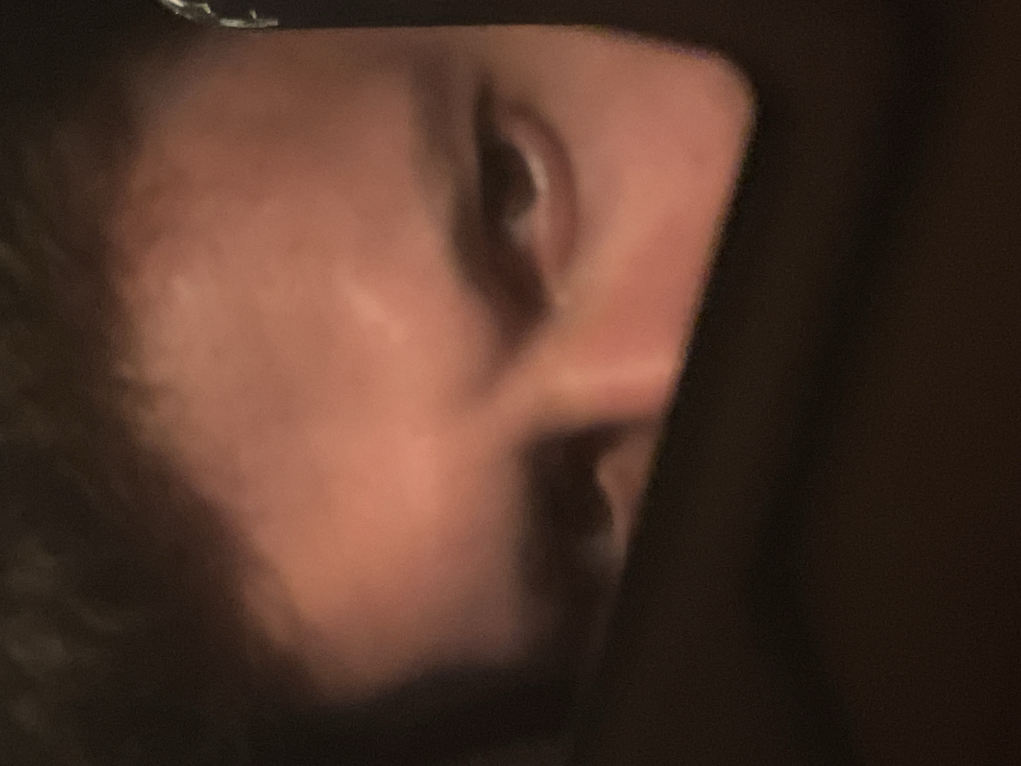 The image is a close-up shot of a person's face in profile. The person's skin is light-toned. Visible features include the nose, ear, and part of the mouth. The lighting is dim. The background is dark and indistinct. There is no information about the location being Razgrad, Bulgaria.