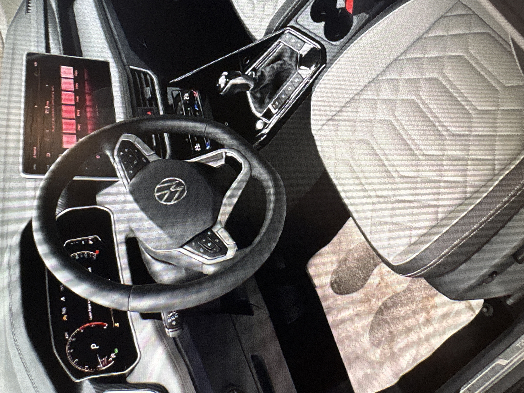 The image shows the interior of a modern car, likely a Volkswagen, given the prominent logo on the steering wheel. The dashboard features a digital instrument cluster and a large infotainment touchscreen displaying what appears to be radio stations or media options. A leather-wrapped steering wheel with control buttons is visible, along with a gear shifter. The seats appear to be upholstered in a quilted material, possibly leather or a high-quality fabric. On the floor mat, there are two distinct shoe prints, indicating recent use of the vehicle. The scene is dimly lit, suggesting it might be evening or inside a garage. The image does not provide any information about its location in Moscow, Russia, or any specific details about people present or their actions beyond the shoe prints.