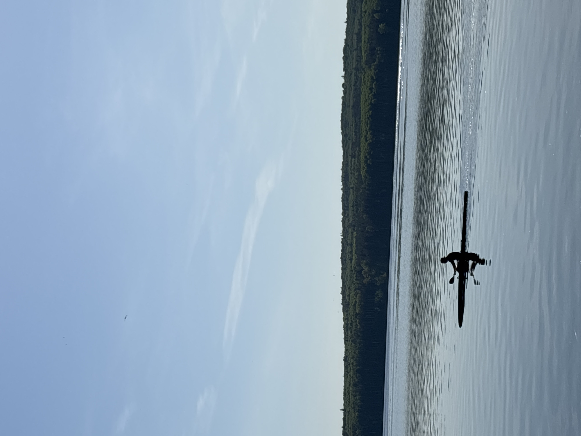 A body of water, possibly a lake, reflects sunlight. A dark line of trees runs along the horizon. A person in a kayak is in the water. The location might be in or near the city of Chaikovsky, Russia, as requested by the prompt.