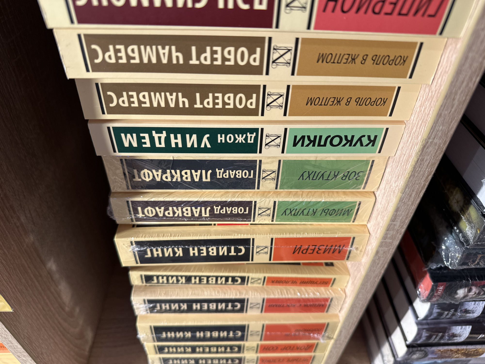 The image shows a stack of books on a shelf, likely in a bookstore in Kazan, Russia. The books are predominantly by authors Robert Chambers, John Wyndham, Howard Lovecraft, and Stephen King. Several copies of the books "King in Yellow" by Robert Chambers, "The Midwich Cuckoos" by John Wyndham, "The Call of Cthulhu" and "The Myths of Cthulhu" by Howard Lovecraft, and "Misery," "Running Man," "Bag of Bones," and "Doctor Sleep" by Stephen King are visible. The books seem to be in new condition, some still wrapped in plastic.