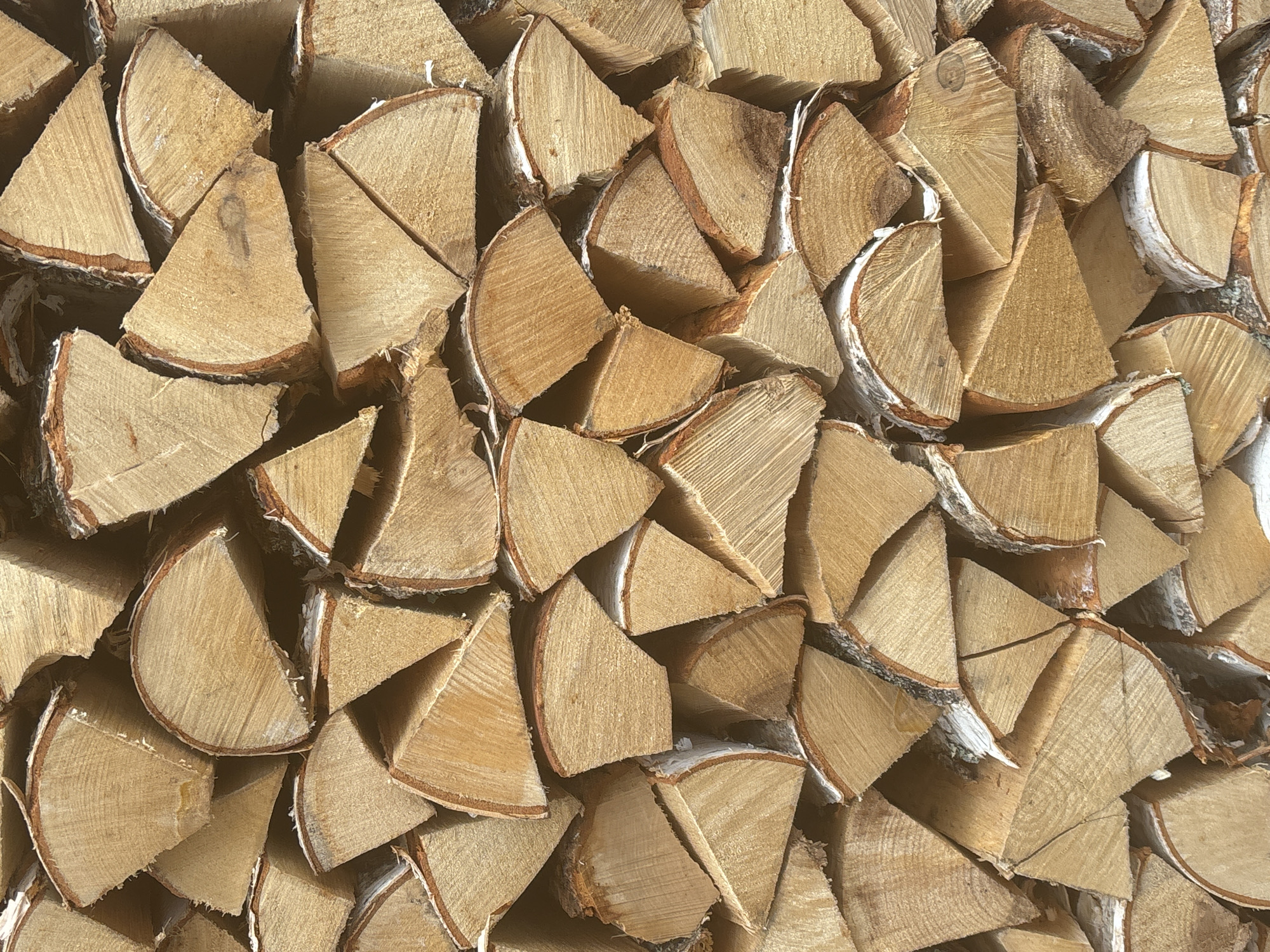 The image depicts a close-up view of a stack of split birch firewood. The pieces are cut into wedge shapes. The wood grain is visible on the cut surfaces. The bark is light-colored. The exact location and any specific context related to the city of Chaikovsky, Russia, is not discernible from the image alone.