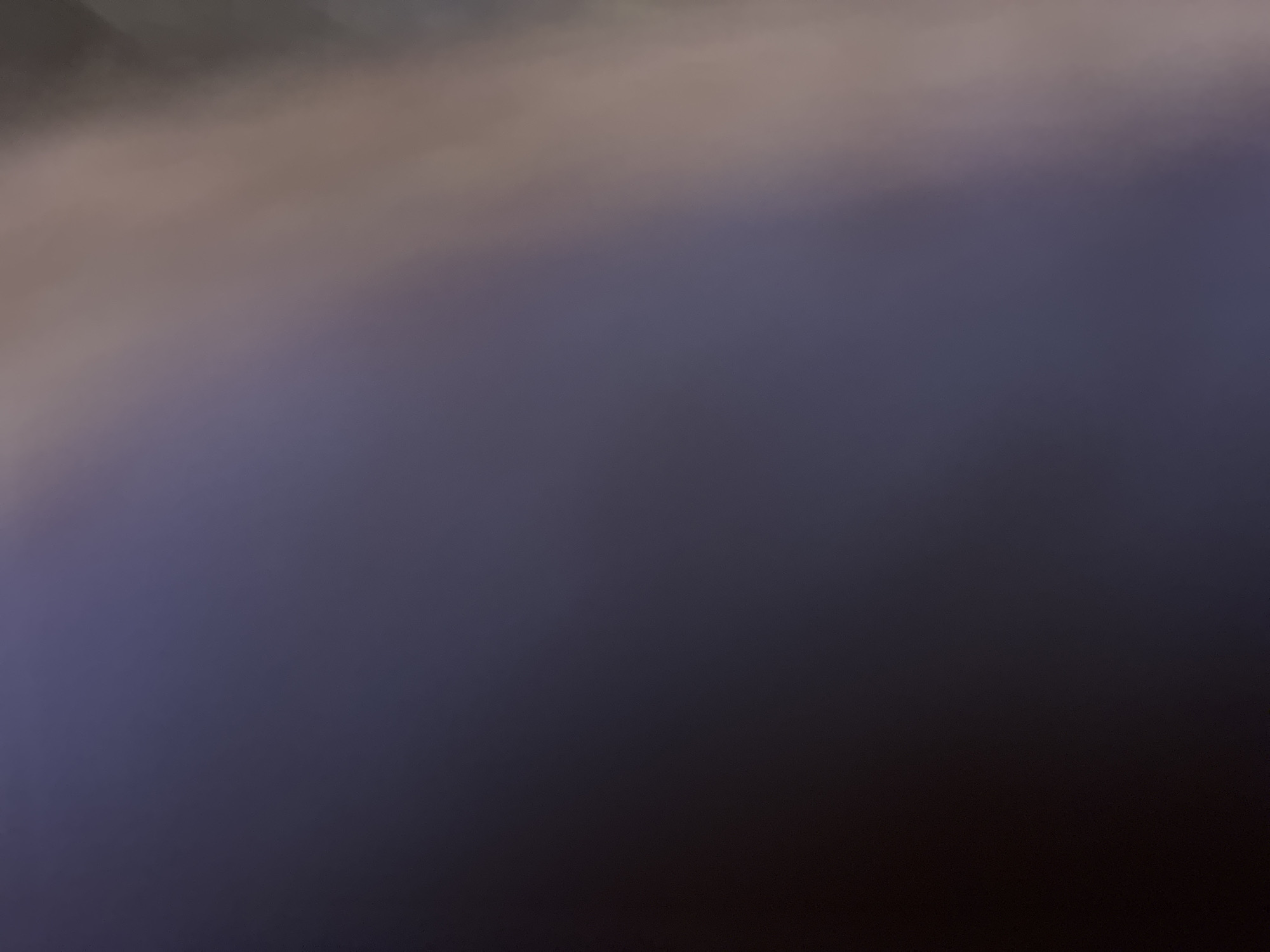 This media file presents a highly abstract and out-of-focus image, characterized by a smooth color gradient. No specific subjects, people, or objects are discernible within the frame. The scene is dominated by a transition from lighter, muted tones in the upper portion to darker, deeper hues towards the bottom and right.
The top and upper-left areas display shades of light brown, grey, and beige, blending downwards into a prominent mid-section of dark blue or deep purple. This cooler tone gradually darkens further, becoming almost black in the bottom-right and lower areas of the image. The entire composition is extremely blurred, resembling a soft, painterly wash of colors rather than a photograph with clear details.
There is no visible activity or event taking place. The soft light and dark color palette suggest a low-light environment, possibly twilight, dusk, or a dimly lit interior/exterior setting, but there are no definitive cues like sunlight or artificial lights. No location-specific details or landmarks are present to connect the image to Sofia, Bulgaria, or any other particular place. There is no visible text. The overall impression is one of a serene, muted, and indistinct visual field.