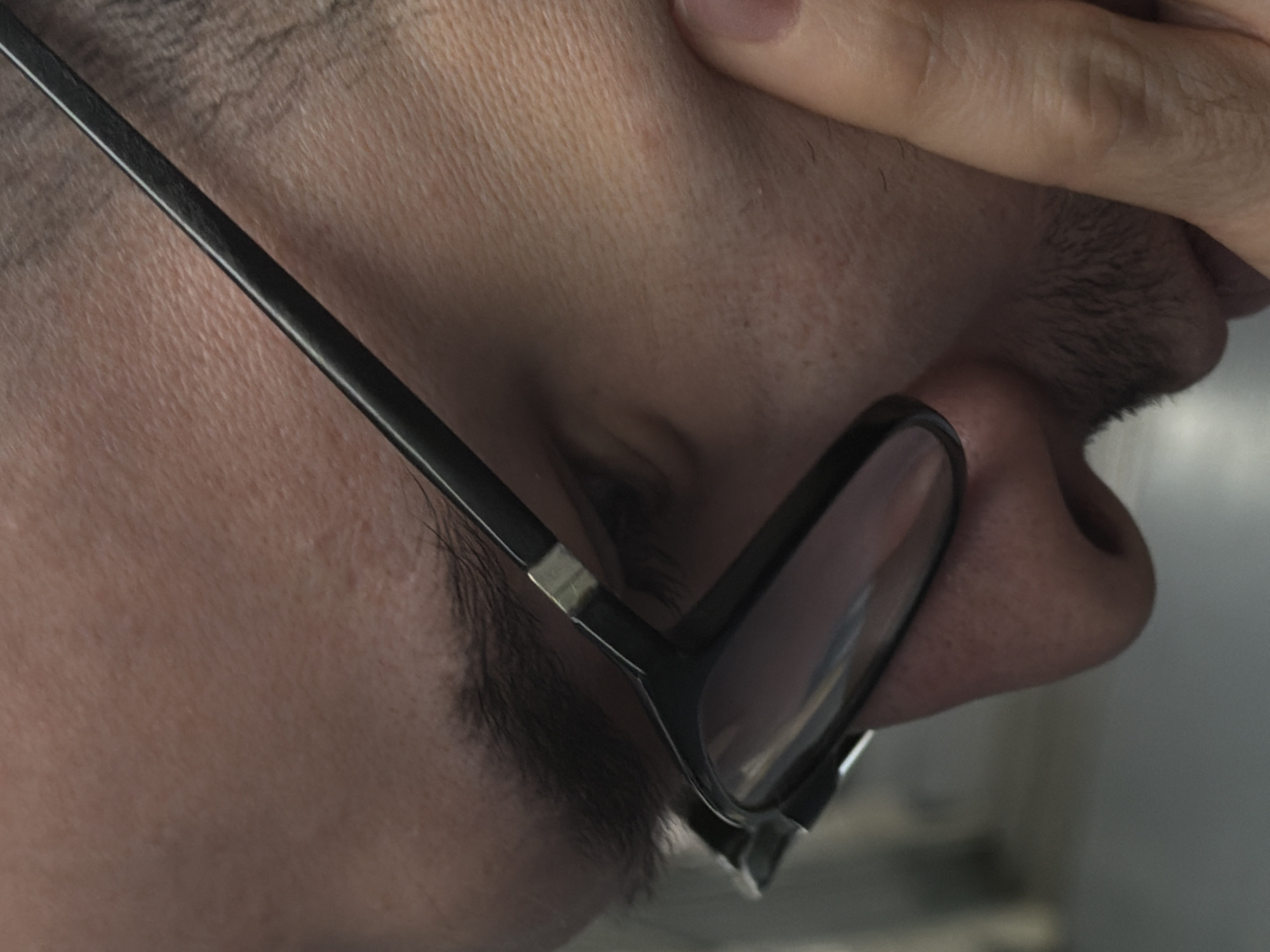 A close-up shot focuses on a person's face, partially obscured by their hand. The individual wears glasses with black frames. Their skin tone appears light. The surrounding environment is indistinct, with a glimpse of a neutral-toned background. The scene doesn't give any geographical information related to Moscow, Russia.