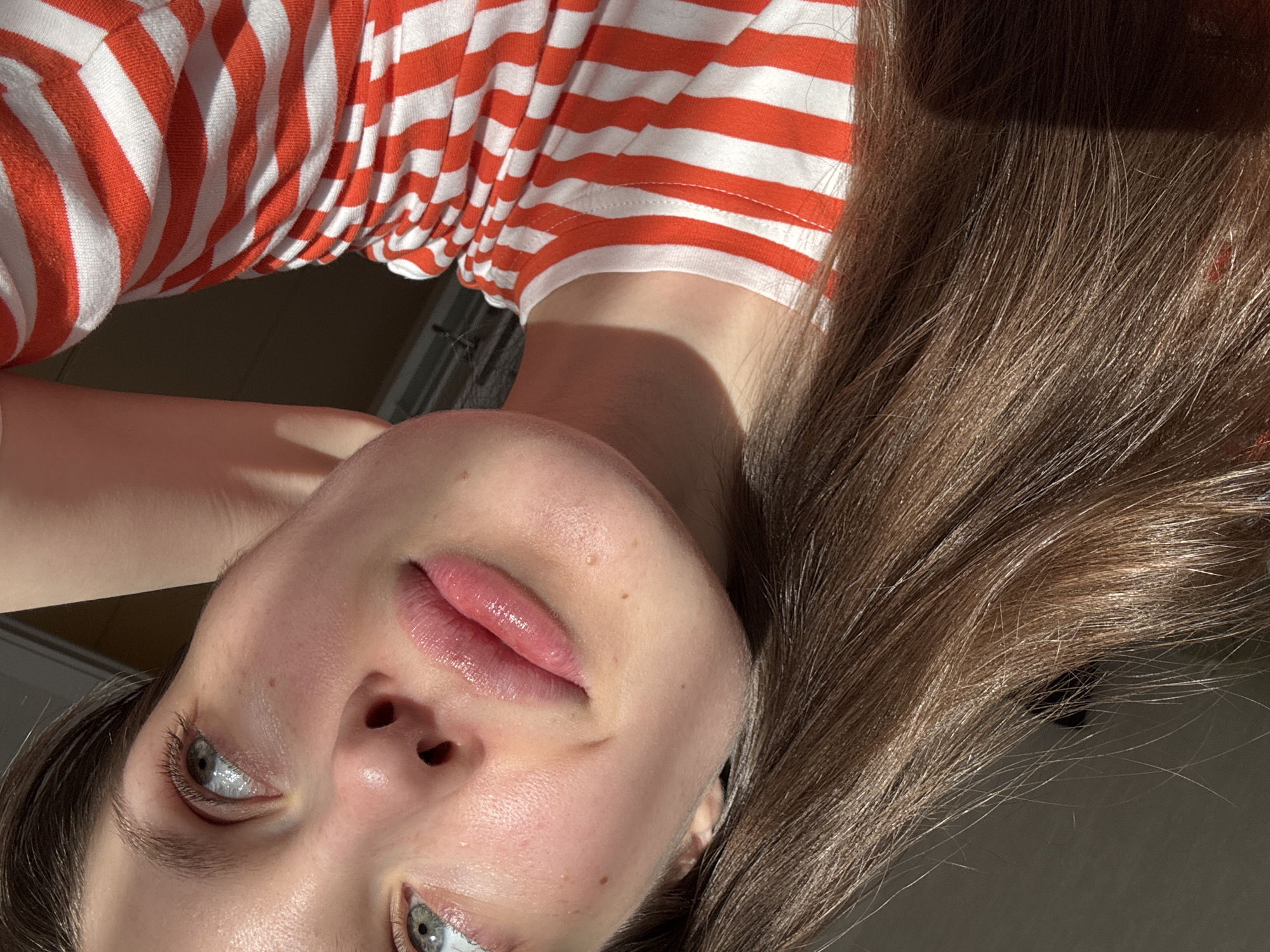 A close-up, slightly downward-angled view of a person's face and upper torso. The person wears a red and white striped shirt. Their hair is brown and falls towards the right side of the frame. The person has fair skin, light-colored eyes, and slightly glossy lips. The background is indistinct but appears to be an indoor setting. There is no indication that the image was taken in Moscow, Russia.