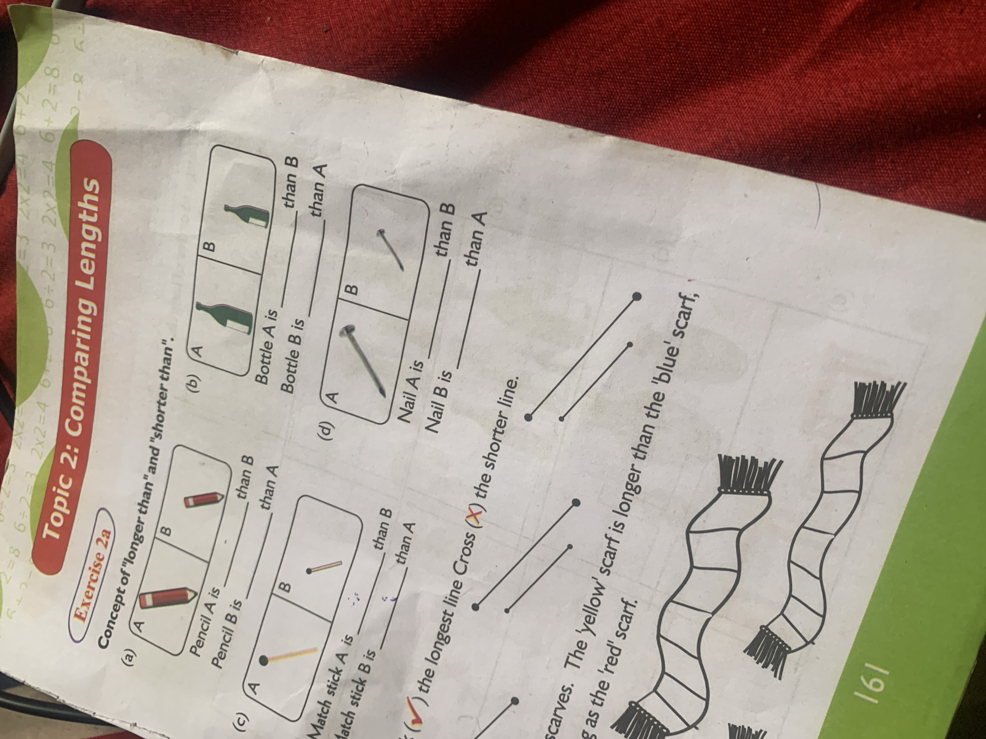 The image shows a page from a workbook titled "Topic 2: Comparing Lengths" and "Exercise 2a". The page contains several exercises for comparing the lengths of objects.
In part (a), two pencils are shown, labeled A and B. The exercise asks to compare the lengths of Pencil A and Pencil B using "longer than" and "shorter than". Pencil A appears to be longer than Pencil B.
Part (b) shows two bottles, labeled A and B. Similar to part (a), the exercise asks to compare their lengths. Bottle A appears to be longer than Bottle B.
Part (c) displays two matchsticks, A and B. The exercise requires comparing their lengths. Matchstick A appears to be longer than Matchstick B.
Part (d) presents two nails, A and B. The exercise asks to compare their lengths. Nail A appears to be longer than Nail B.
Below these parts, there are three lines shown, with a checkmark next to instructions to mark the longest line and a cross next to instructions to mark the shorter line.
Further down, there is text describing scarves. It states, "The 'yellow' scarf is longer than the 'blue' scarf." Two scarf illustrations are provided, with one appearing longer than the other.
The page number "161" is visible at the bottom left corner. The background of the image is a red fabric.
There is no information in the image that could indicate its location in Jauro Yinu, Nigeria.