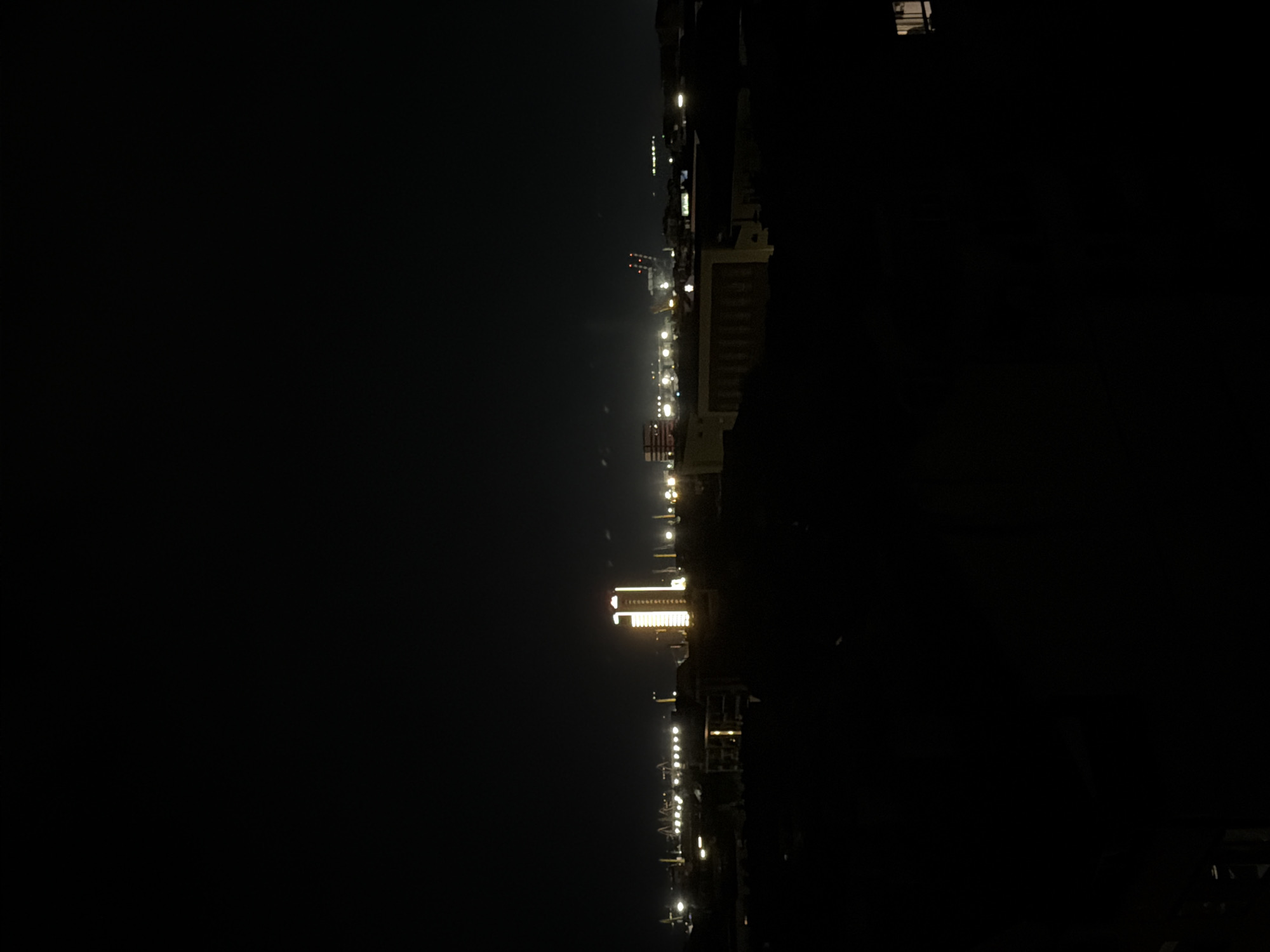 The image depicts a night scene in Burgas, Bulgaria, showing the skyline illuminated by city lights. The view includes lit structures, possibly buildings and infrastructure, stretching along the horizon line. Specific details are limited due to the darkness, but the scene suggests an urban environment with artificial lighting.