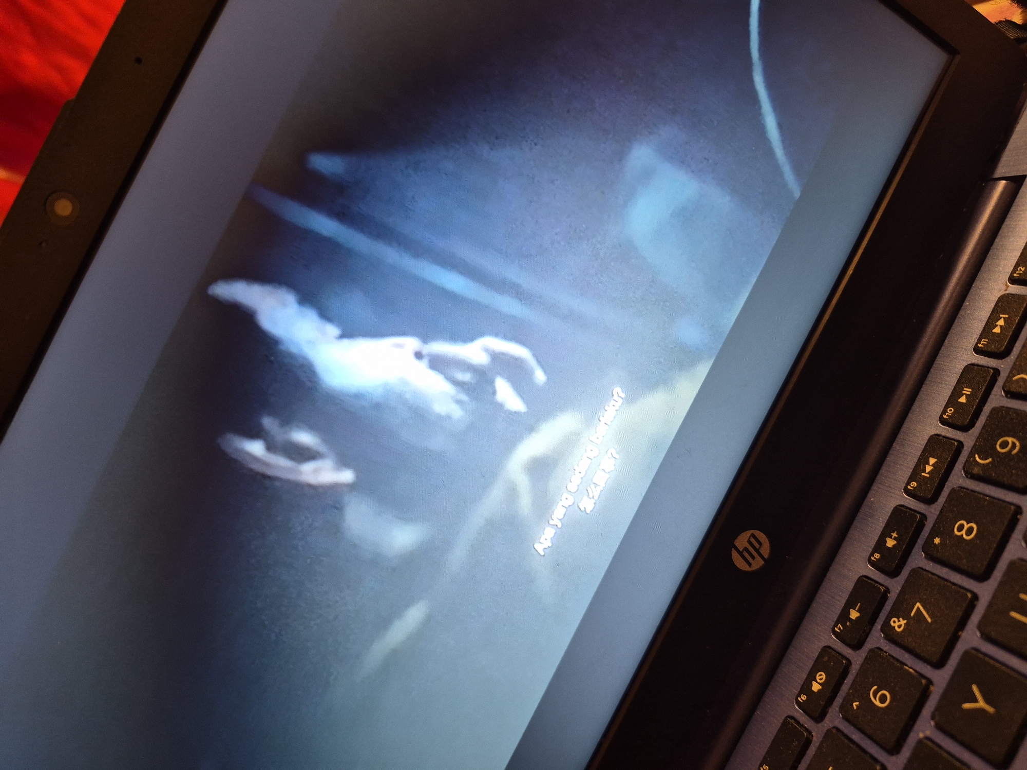 The image shows a laptop screen displaying a video with subtitles. The subtitles are in what appears to be Indonesian and Chinese. The video itself is abstract and features bright, glowing forms against a dark, blurry background. The laptop is open, and part of the keyboard, showing the HP logo, is visible in the foreground. The image is taken from an angle that emphasizes the screen and the keyboard. There is no discernible information within the image that could suggest a specific location in the city of Sandwell, United Kingdom.