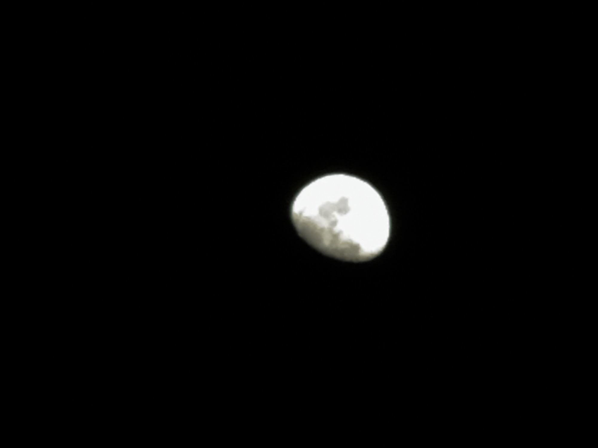 A night scene shows the moon as a prominent celestial body against a completely dark background. The moon is partially illuminated, with the light concentrated on the right side, suggesting it is in its waxing gibbous phase. No other objects or individuals are visible. There is no location data available.