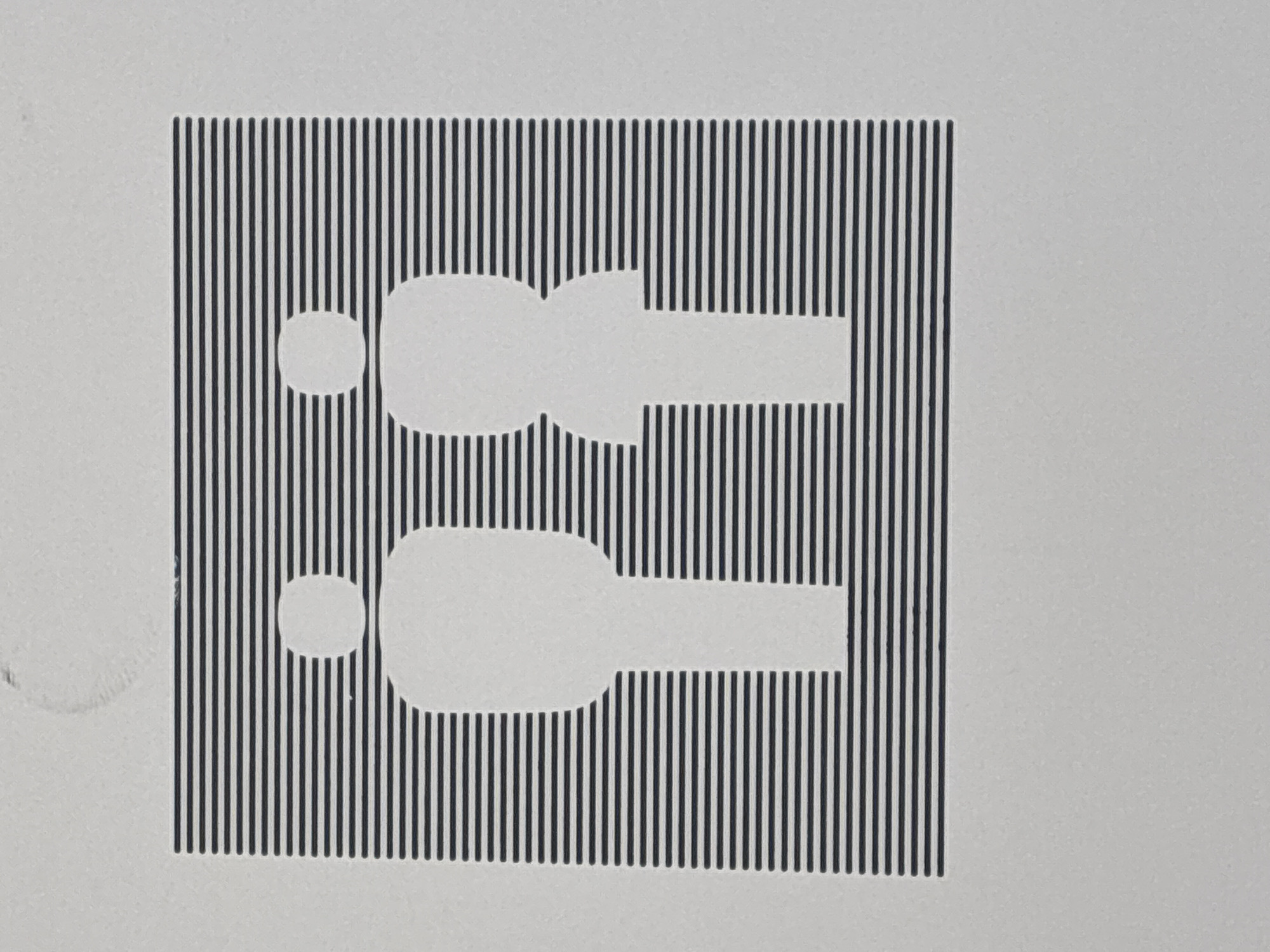 The image shows a restroom sign with stylized figures of a man and a woman. The figures are depicted in silhouette, with the man on the left and the woman on the right. Both figures are white and are positioned in front of a background of horizontal black lines. The sign is printed on a light gray textured surface. The sign is located on the exterior of a building in Schönefeld, Germany.