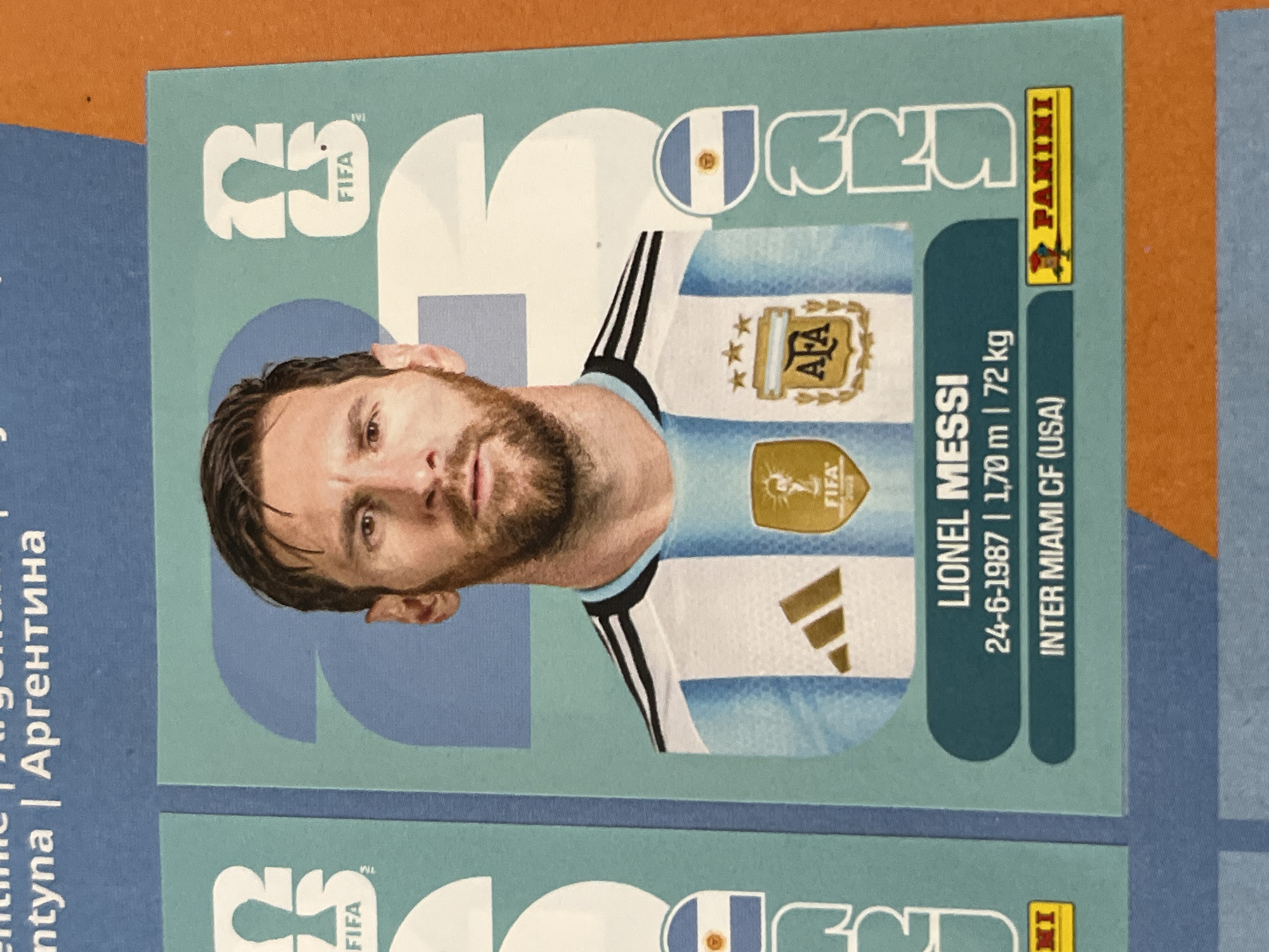 The image shows a soccer trading card of Lionel Messi. The card features an image of Messi in his Argentina national team jersey. The card displays the FIFA and AFA logos. Text on the card states Messi's name, birthdate (24-6-1987), height (1.70m), weight (72kg), and his current club, Inter Miami CF (USA). The Panini logo is also visible.