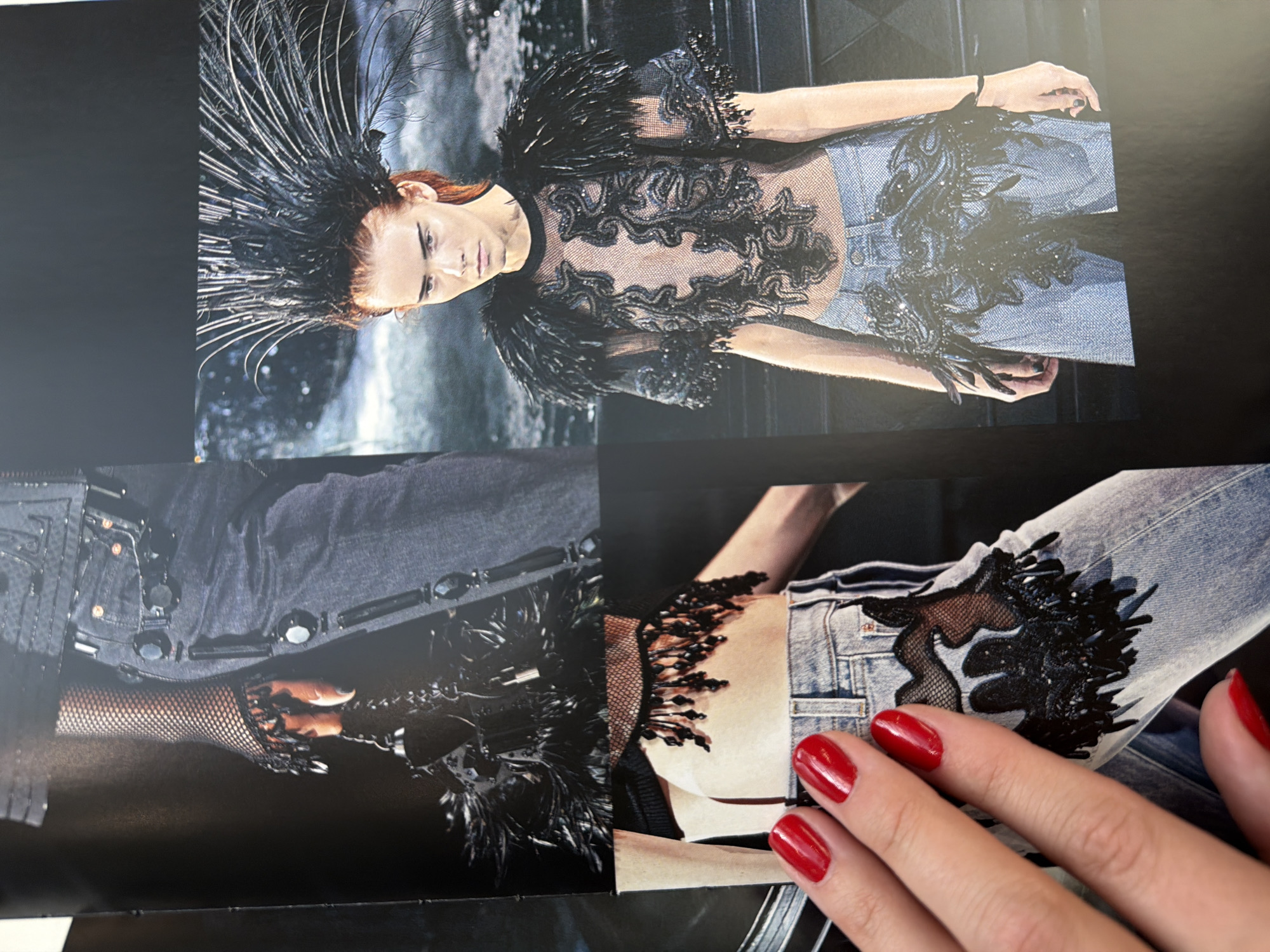 The image depicts a printout of a fashion editorial. The main subject is a fashion model with red hair, wearing a sheer top with black feather and sequin embellishments. She also wears jeans. A separate picture on the printout shows a close-up of the same outfit on jeans and on fishnet gloves, showing further detailing with black embellishments. A hand with red nail polish rests on the printout, near the close-up image of the jeans. The location of Izhevsk, Russia is not discernible from the image.