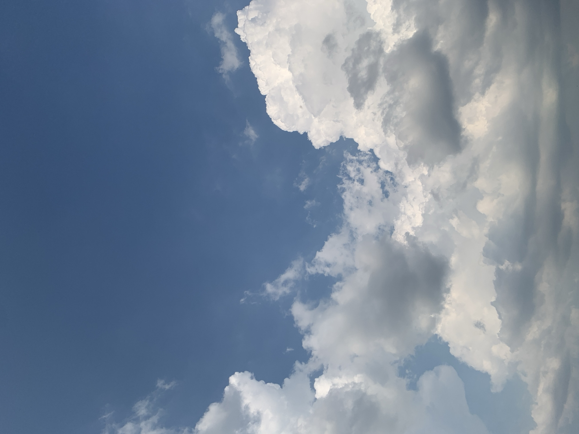 The image shows a sky filled with clouds. The sky is a deep blue and appears to be a bright, sunny day. The clouds are white and fluffy, with some areas appearing darker and more gray, suggesting they might be thicker or on the verge of rain. There are no people, subjects, objects, or actions visible in the image. The scene depicts a natural sky formation, and no specific location in Kolomyia, Ukraine can be identified from the image itself.