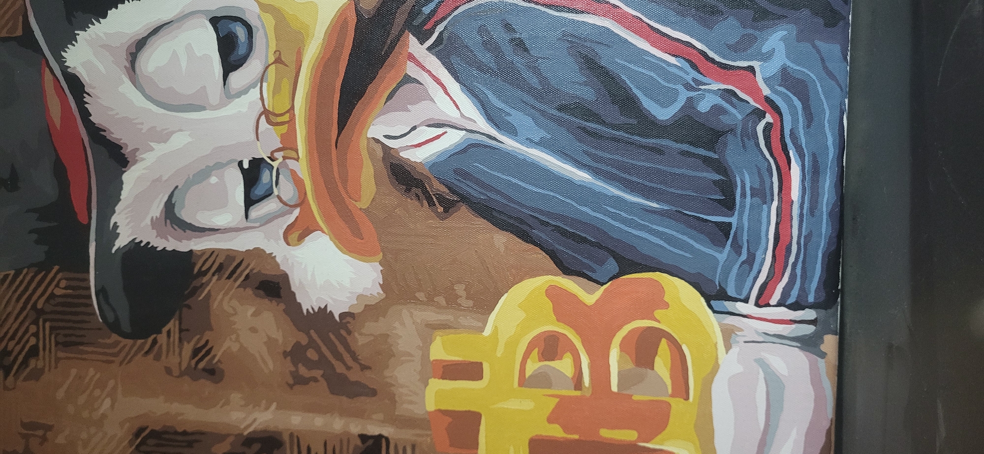 The image shows a section of a paint-by-numbers artwork depicting a stylized character with elements suggestive of the city of Moscow, Russia. The character is a white animal-like figure wearing spectacles and a black hat with a red band, set against a backdrop of what appears to be a stylized Russian military jacket. An object resembling a children's toy or seat with cut-out openings is visible, with colours of yellow and orange. The background and foreground contain brown and beige abstract patterns. The style of the work is flat and graphic, with bold outlines.