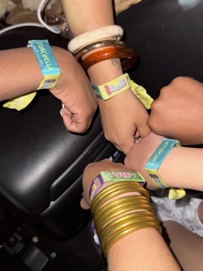 Four arms and hands are visible in the image, each wearing a wristband indicating access to the Coachella music festival, which is held annually in Indio, United States. One wristband is identified as "VIP". The individuals are also wearing various bracelets. The setting appears to be indoors, possibly inside a vehicle, given the presence of a dark interior with what looks like leather seating. The composition is tightly framed around the hands and wrists.