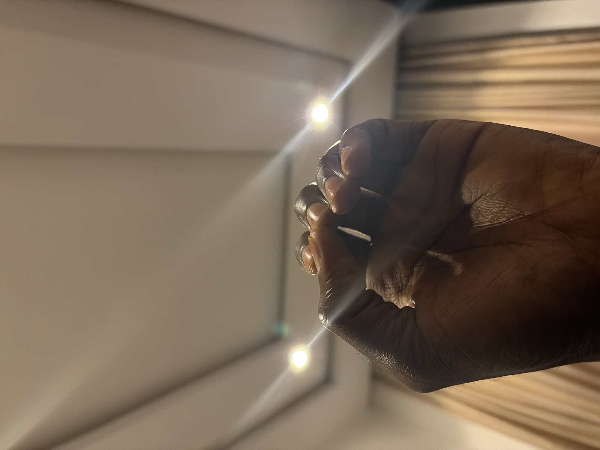 A human hand is positioned in the foreground, obscuring a portion of the background. The background consists of a light-colored surface with horizontal lines. Two bright, spherical lights are visible, positioned above and below the hand. The location of the scene is unknown; no detail in the image suggests that it is the city of Jos, Nigeria.