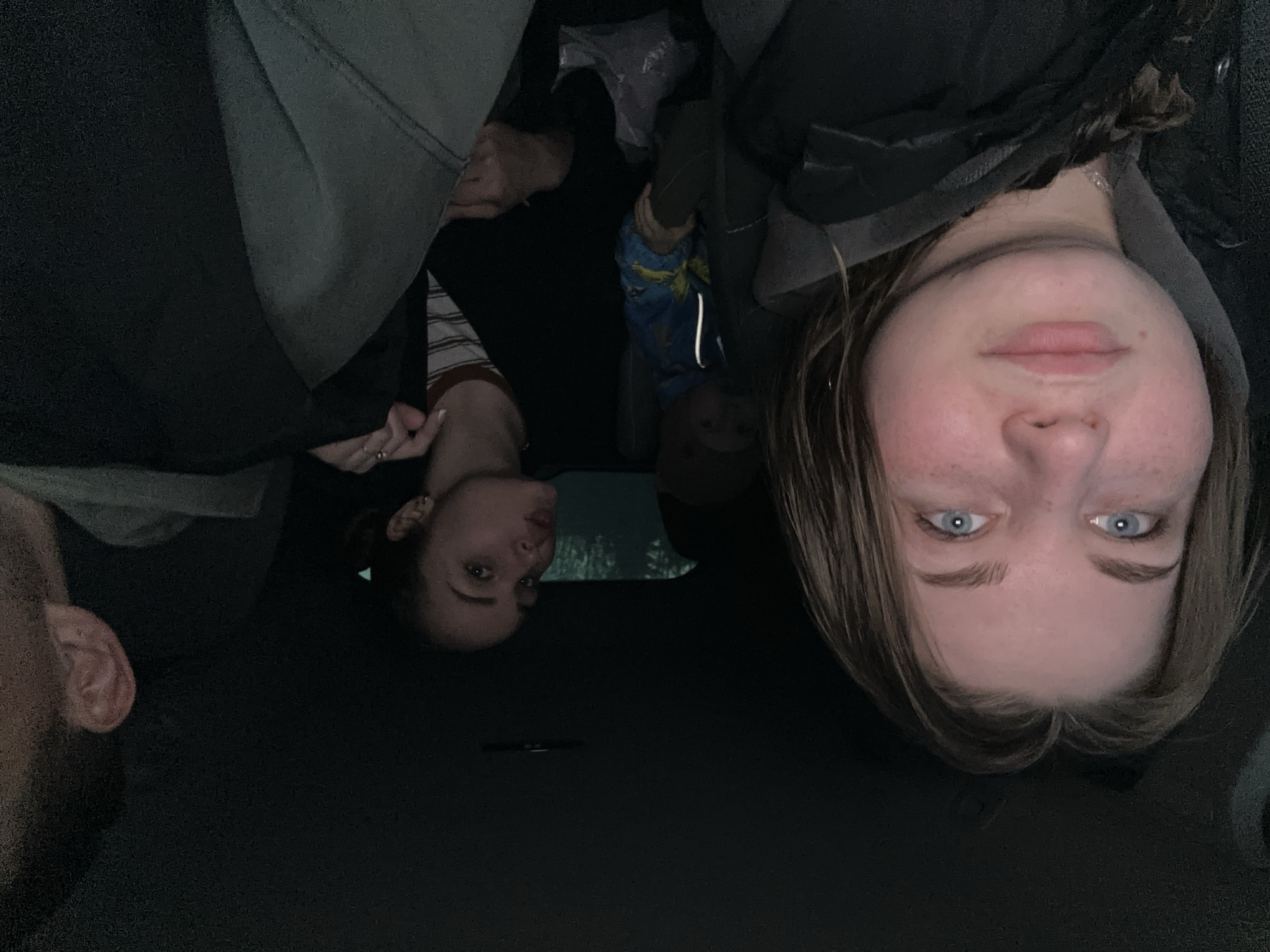 The image depicts a group of individuals inside what appears to be a vehicle. The individuals include a blonde female, brunette female, an individual in a blue and yellow jacket and a man with a partial view of the side of their head. The location is unknown, but it is alleged to be in Chaikovsky, Russia. No specific actions or interactions are clearly discernible beyond their presence within the confined space. The environment inside the vehicle is dark.
