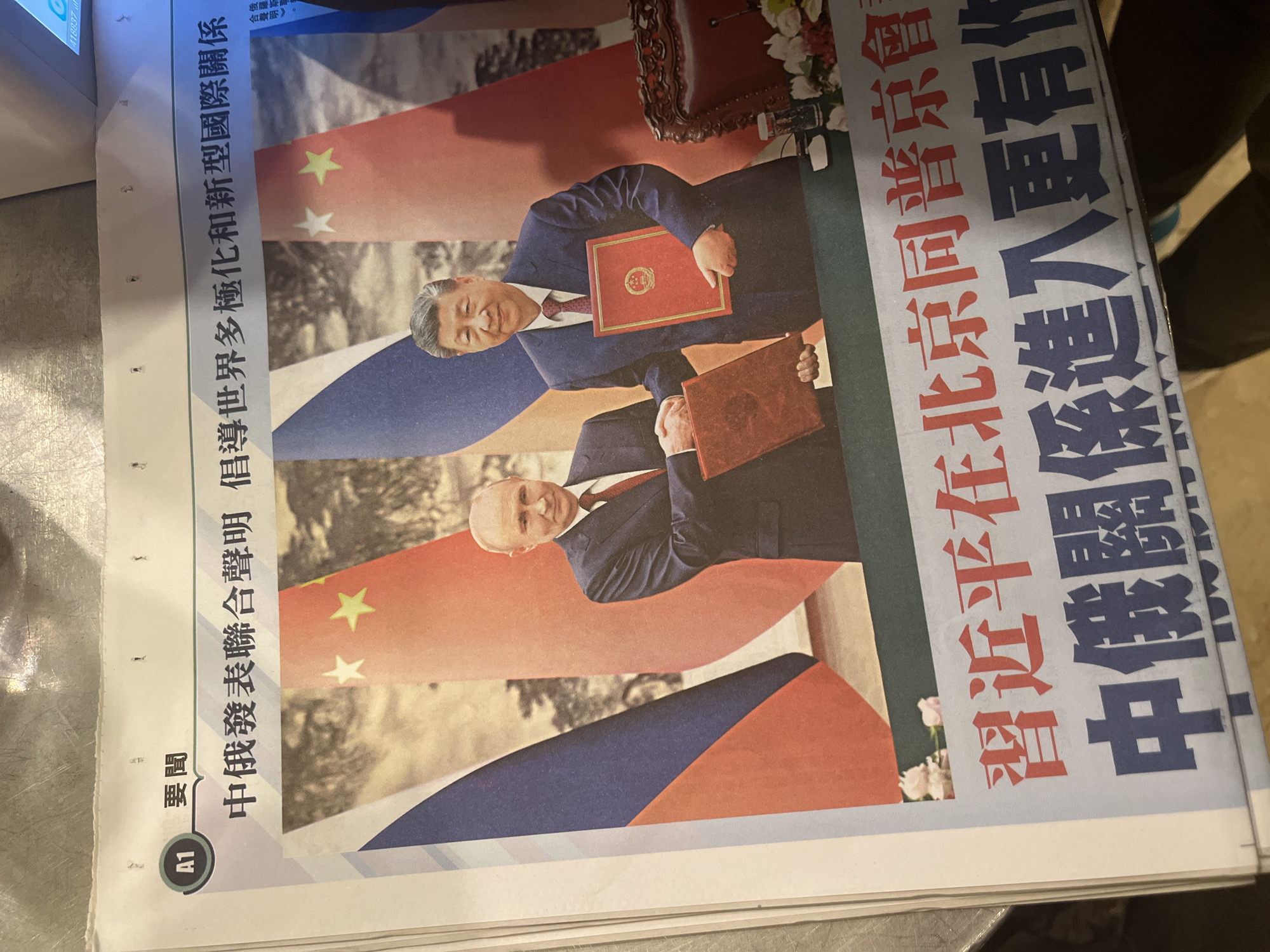 The image shows a newspaper with a front-page article. The headline reads "China and Russia issue a joint statement advocating a multipolar world and a new type of international relations." The headline is in Chinese. Below the headline is a large color image featuring digitally imposed portraits of Xi Jinping of China and Mike Pence of the USA. Behind the portraits are flags of China and the USA. The location is Hong Kong.