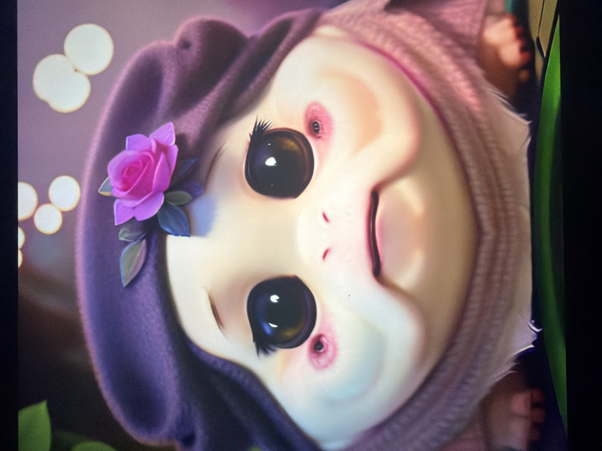 The image is a close-up, animated, portrait-style shot of a character. The character has large, dark, expressive eyes with long, dark eyelashes. The character's face is pale yellow with pink blush marks on the cheeks, and faint red circular marks below each eye. The character is wearing a purple beret adorned with a pink rose and green leaves. A pink knitted garment is visible around the character's neck and shoulders. The background is blurred with bokeh lights, suggesting a soft, possibly nighttime, setting. The character appears to be looking directly at the viewer with a slightly sad or concerned expression. The overall aesthetic is soft, whimsical, and visually appealing. There is no visible indication of any specific location in the city of Kyiv, Ukraine, or any discernible interaction or action occurring.
