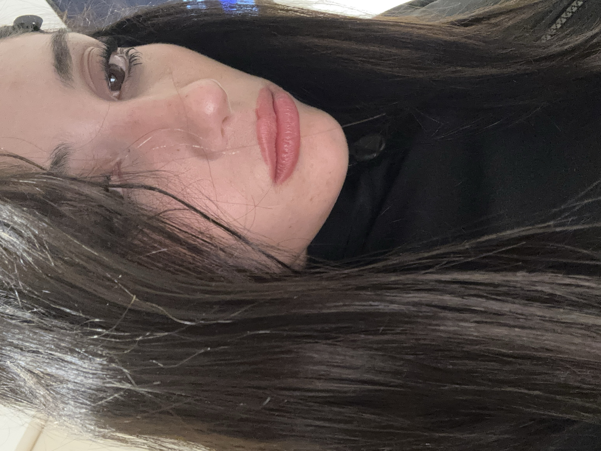 A close-up image of a woman's face, rotated counterclockwise. Her dark hair is spread around her face. She has light skin, dark eyes, and is wearing lipstick. The background is indistinct, suggesting a dark garment or setting. There is no discernible information about the location being Buenos Aires, Argentina.