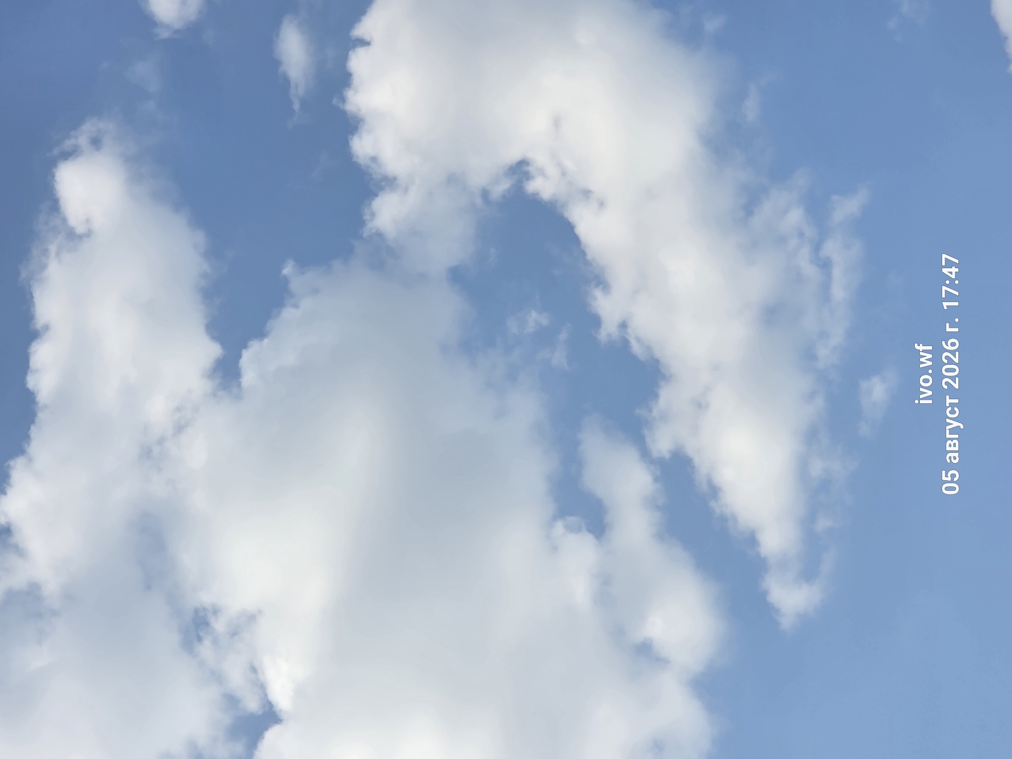 The image displays a sky with scattered white clouds against a bright blue background. In the lower right corner, there is a timestamp overlay that reads "ivo.wf 05 август 2026 г. 17:47". This indicates the image was taken on August 5, 2026, at 5:47 PM. There are no people, subjects, objects, or actions visible in the image besides the sky and the text overlay. The scene is outdoors, and there is no indication of the city of Chal, Bulgaria.