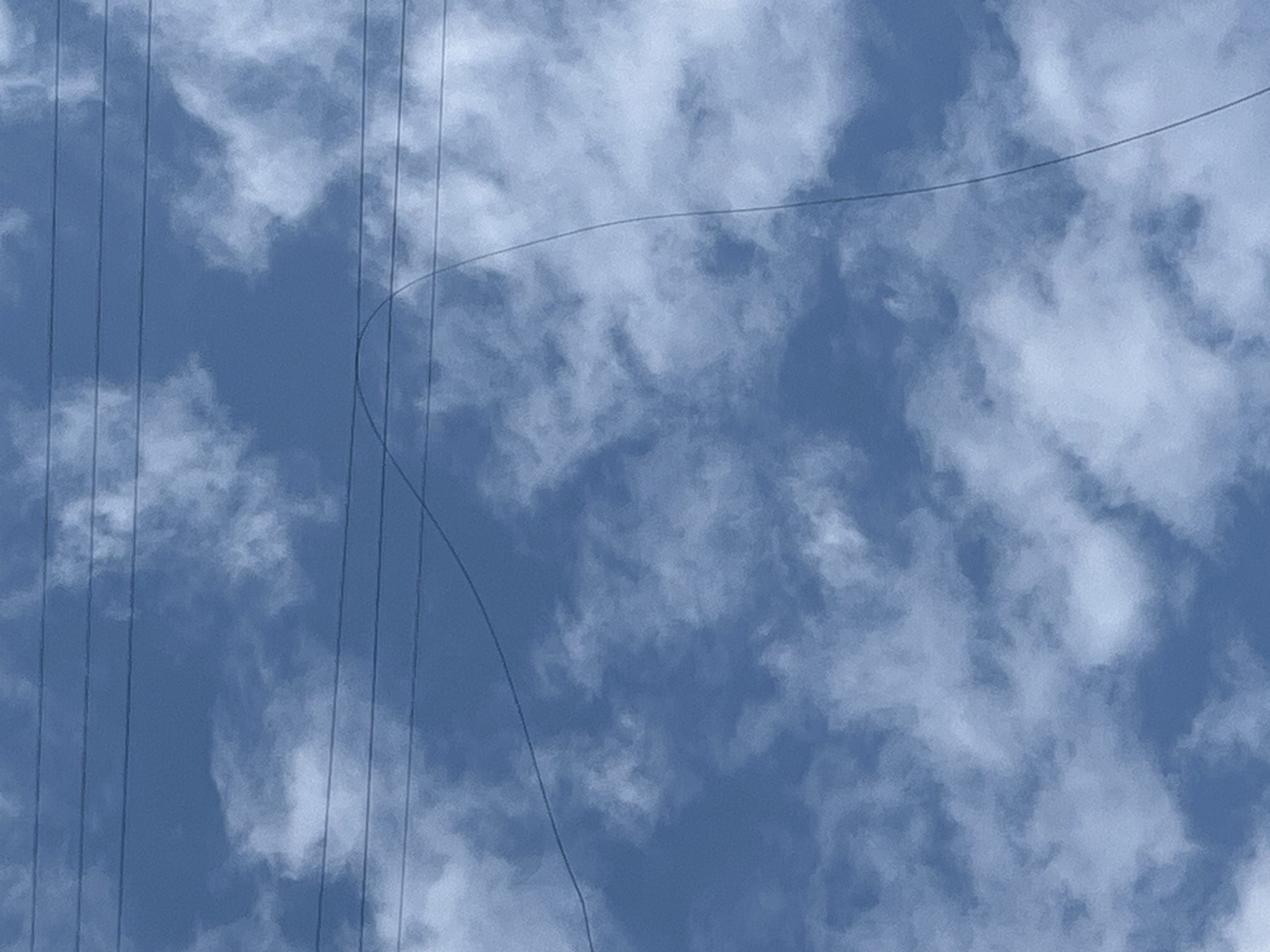 The image captures a sky with scattered clouds, suggesting an outdoor setting. Multiple horizontal power lines stretch across the frame. One power line is notably bowed, creating a curve in its path. The overall impression is of a clear day with visible infrastructure against a natural backdrop. The specific location in Kyiv, Ukraine cannot be determined from the visual information present.