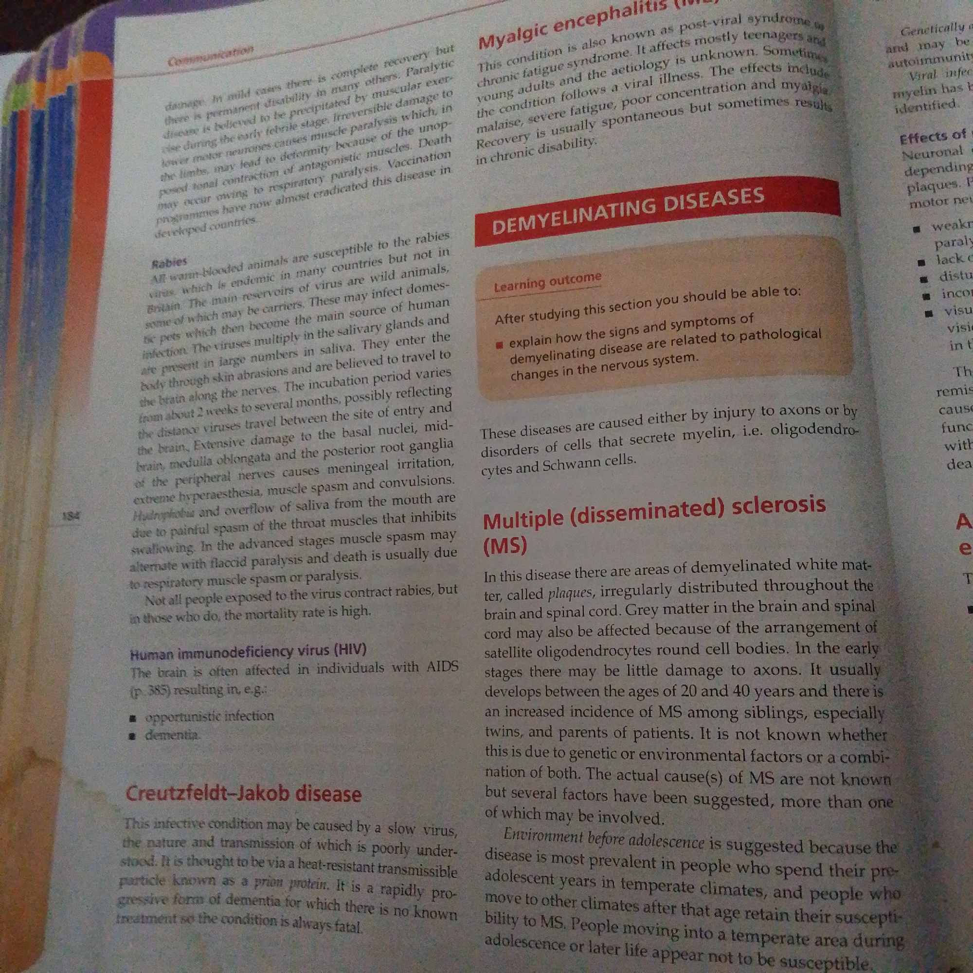 The image is a close-up of an open textbook page with a slightly textured, matte finish. The text is printed in black ink with bolded headings in red and blue. The page is from a biology or medical textbook, discussing various diseases.
Subjects: The primary subjects are the printed words and headings within the textbook. There are no people, objects, or scenes depicted in the photograph itself, only the content of the book.
Activity or event: The "event" is the act of reading or studying the textbook. The content suggests the material being studied relates to diseases and their characteristics.
Notable details: The text includes headings like "Communication," "Myalgic encephalitis," "DEMYELINATING DISEASES," "Multiple (disseminated) sclerosis (MS)," "Human immunodeficiency virus (HIV)," and "Creutzfeldt-Jakob disease." There are also bullet points detailing symptoms and learning outcomes. The page number "184" is visible. The lighting appears to be from above and slightly to the left, casting subtle shadows and highlighting the texture of the paper.
Visible text: The image contains a significant amount of legible text, including:
- "Communication"
- "Myalgic encephalitis"
- "DEMYELINATING DISEASES"
- "Learning outcome"
- "Multiple (disseminated) sclerosis (MS)"
- "Human immunodeficiency virus (HIV)"
- "Creutzfeldt-Jakob disease"
- And detailed descriptions of these medical conditions.
The location context of Jalingo, Nigeria, is not discernible from the image itself.
