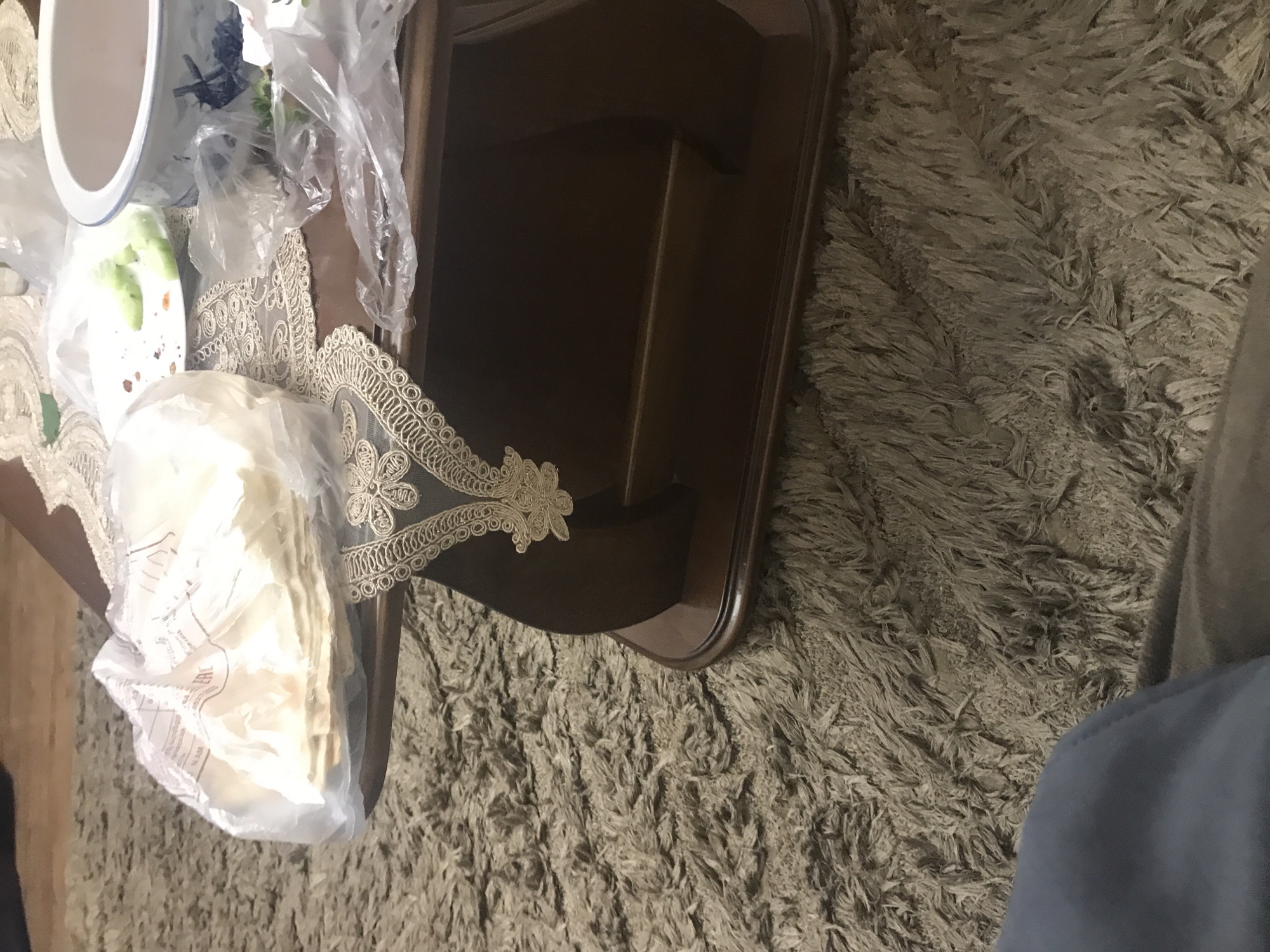 The image depicts a table placed on a shag carpet. On the table, there is a bowl, a plate of food, and several plastic bags. The location is unknown and there are no people visible.