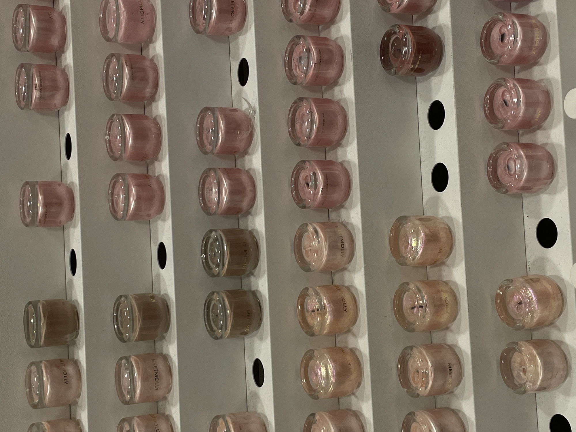 The image displays multiple rows of small, clear glass containers with metallic or pearlescent liquid contents, likely nail polish or similar cosmetic products. The containers are arranged on white tiered shelves, suggesting a retail or display setting. Some of the containers have visible text labels, and the colors of the contents vary, including shades of pink, brown, and a reddish-brown. The overall impression is of a well-organized product display. The image does not provide enough visual information to determine a specific location within Davao City, Philippines.