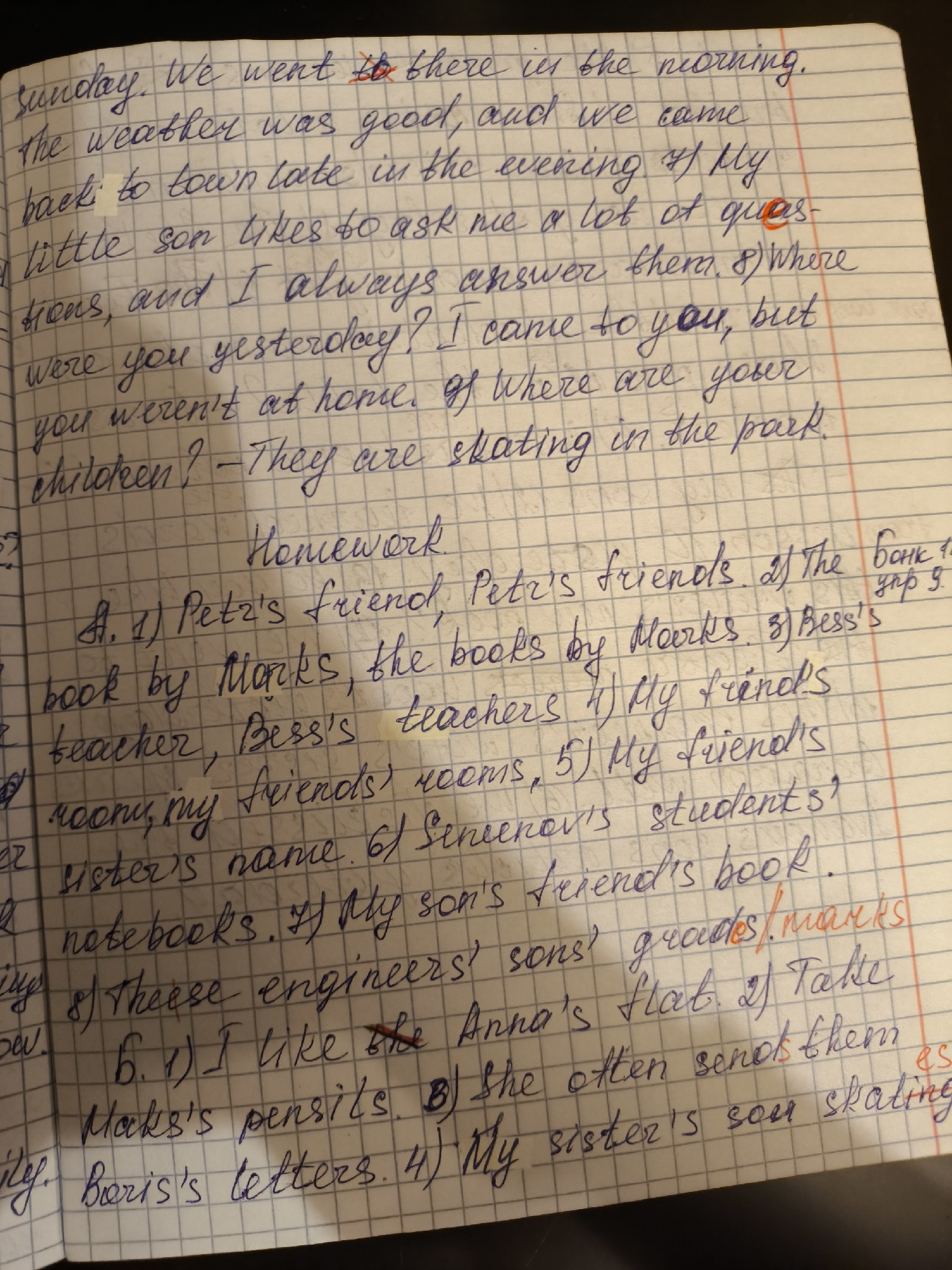 The image is a close-up shot of a handwritten page from a notebook with grid lines. The text is written in blue ink and contains examples of English grammar exercises. There are corrections in red ink. The page is titled "Homework" and contains sentences with possessive nouns.