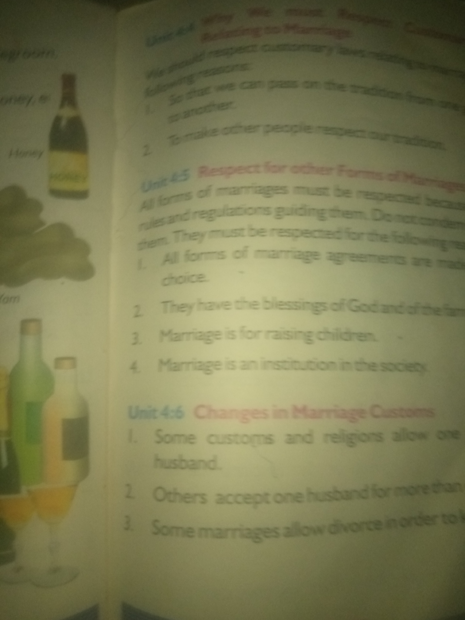 The image shows an open book with text and illustrations. The text discusses marriage customs. On the left side of the page, there are illustrations of bottles and glasses, possibly representing drinks or a still life. The text on the right side of the page is divided into sections labeled "Unit 4.4" and "Unit 4.5," with numbered points under each. The content discusses respecting customary laws and forms of marriage, and then shifts to changes in marriage customs. The overall scene appears to be a classroom or library setting, with the book lying flat on a surface. There is no information about a specific city or location within the image.