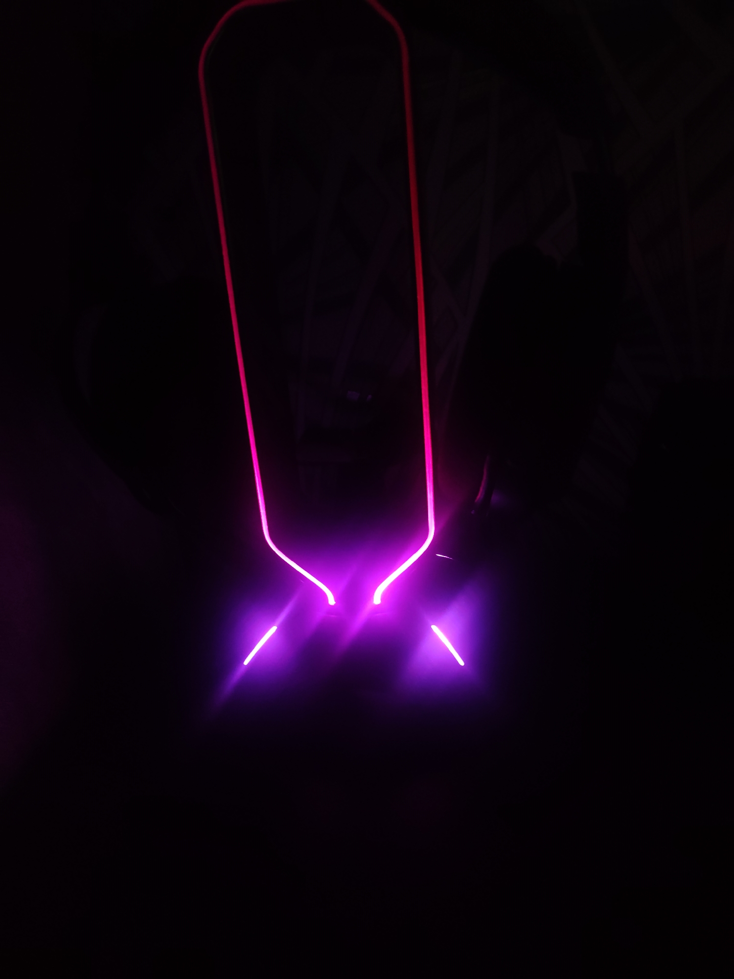 In a dimly lit, indoor environment, a neon light fixture glows with vibrant pink and purple hues. The fixture, shaped like an inverted elongated U with two short, straight lines extending downwards from the bottom corners, is positioned against a dark background. The light emits a bright glow, illuminating the surrounding darkness. The scene is devoid of people and any discernible urban context in Borova, Ukraine, or any other location. The focus is solely on the luminous object.