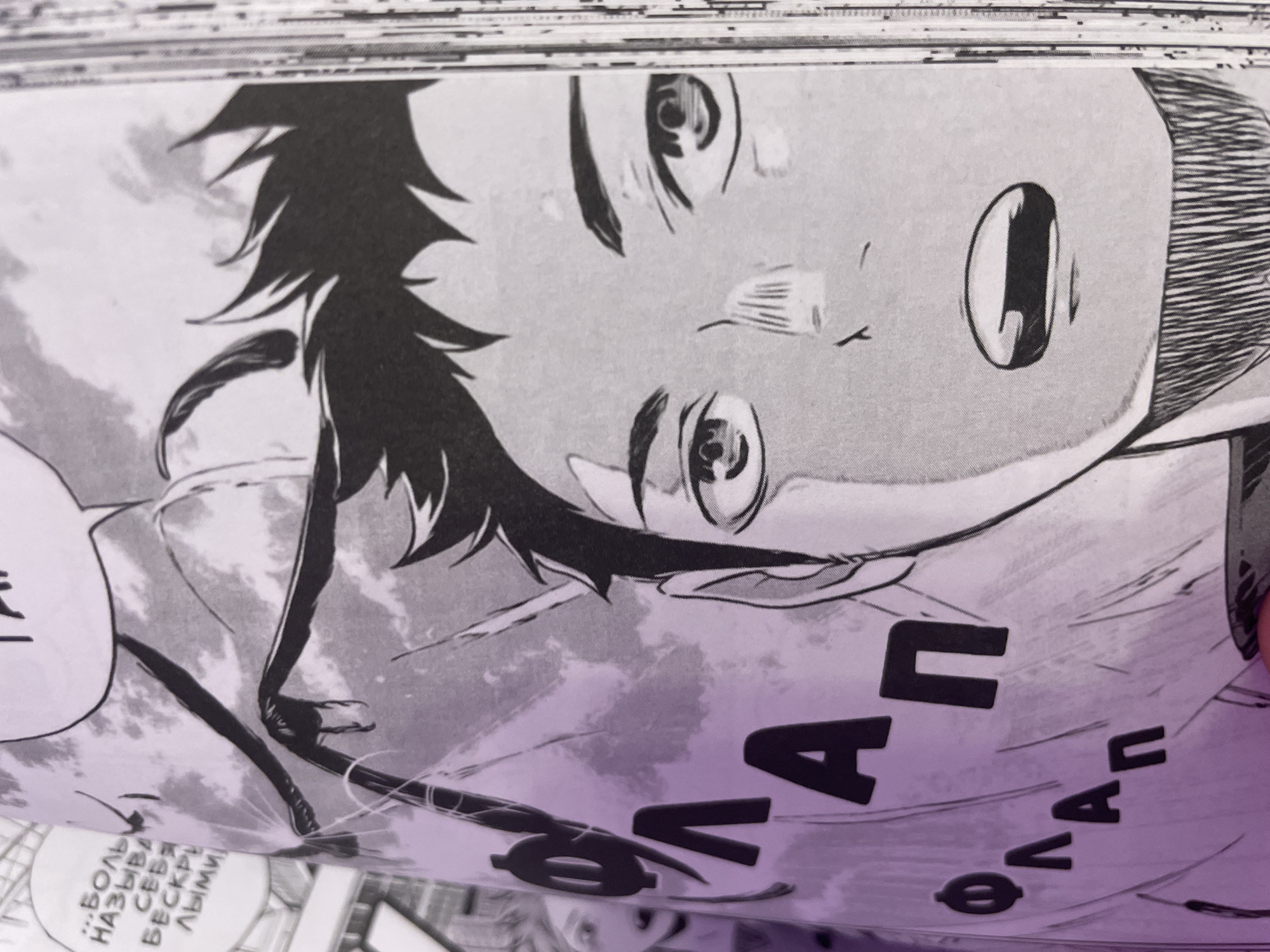 The image shows a close-up of a manga panel. A young male character with spiky black hair and wide eyes is depicted from the chest up. He has a surprised or shocked expression with his mouth open. In the background, behind the character, there are stylized Japanese text elements in large, bold lettering. One of these elements appears to be the word "ФЛАП" (FLAP in Russian), repeated. To the left of the main character, another character's face, also drawn in manga style with blondish hair and a similar expression, is partially visible. The scene is predominantly black and white, with a purple overlay on the left side of the image where the text is located. The overall composition suggests an action or dramatic moment within a narrative. The image does not contain any visual elements that would allow for its location to be identified as Ladozhskoe Ozero, Russia.