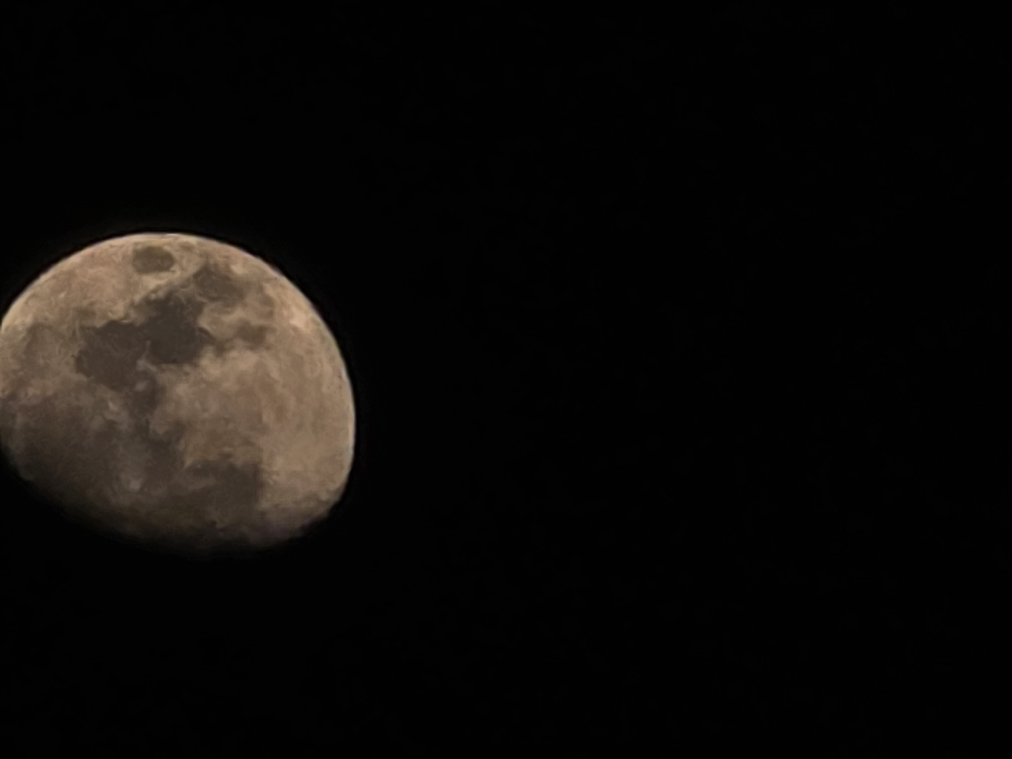 A partially illuminated moon hangs in a dark sky. The moon's surface displays variations in light and shadow, suggesting craters and other topographical features. The scene is devoid of any urban or natural landmarks, making it impossible to determine a specific location within Yambol, Bulgaria, or any other city.