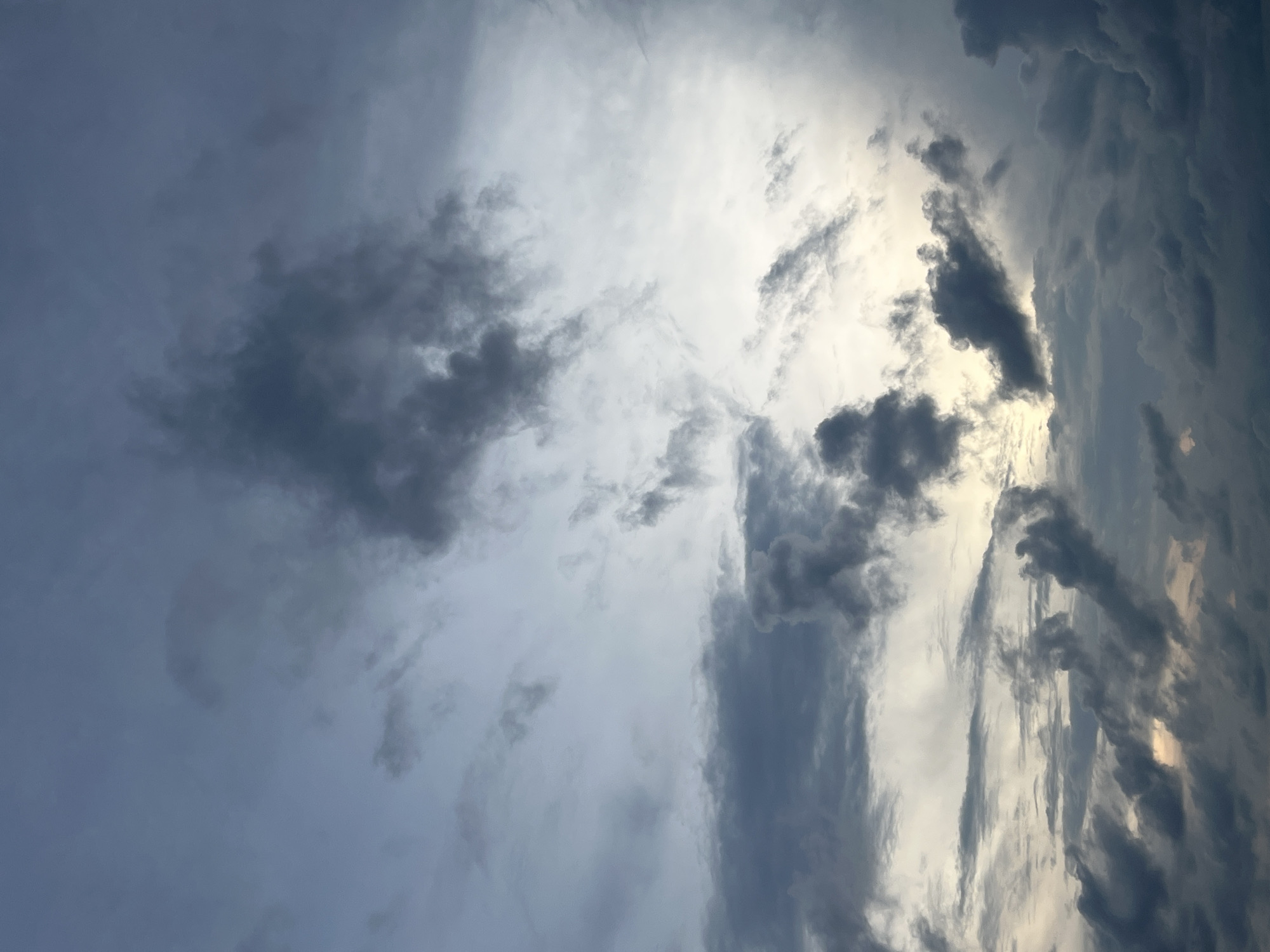 This is a photograph of a cloudy sky. The clouds are dark and appear to be gathering, suggesting an approaching storm or inclement weather. The lighting is dim, and there is a sense of moodiness or drama created by the contrast between the dark clouds and the lighter areas of the sky where the light is breaking through. The image is abstract and focuses entirely on the sky, with no discernible elements of a city or specific location.