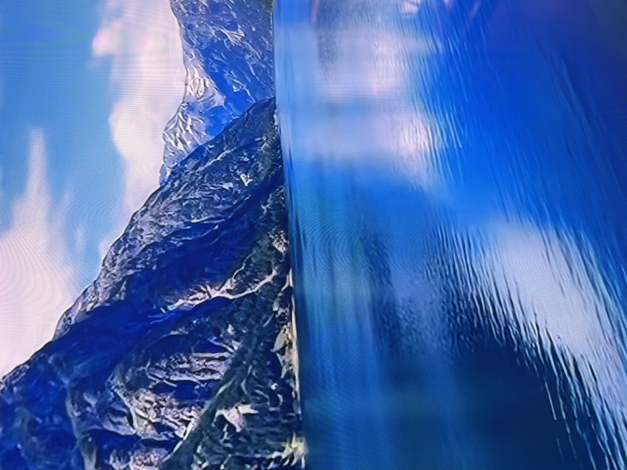 The image depicts a mountainous landscape with a waterfall. The left side shows a rugged, rocky mountain with blue and gray tones, partially obscured by clouds or sky. To the right, a waterfall cascades down, displaying vertical streaks and varying shades of blue. The image does not contain enough details to identify a specific location in Sofia, Bulgaria or information about people, objects, or actions.