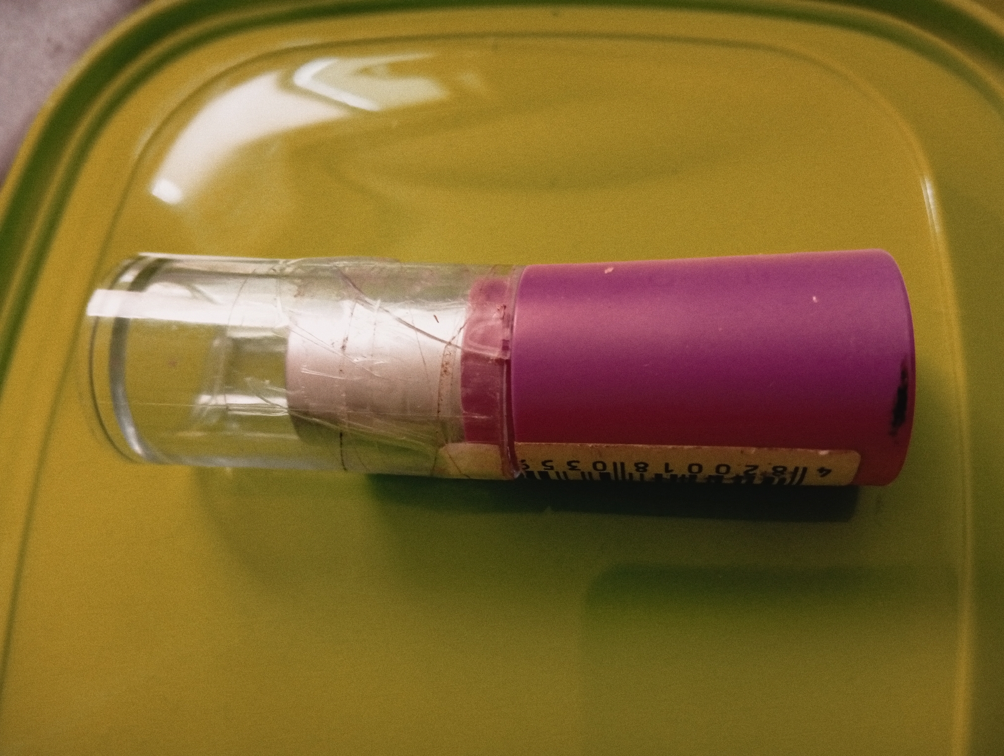 A partially empty clear glass container with a cracked surface sits horizontally on a light green plastic tray. The container is attached to a pink cylindrical component with a barcode sticker adhered to it. The barcode numbers are partially visible. The tray appears to be on a flat surface. The location is not evident from the image and cannot be determined to be in Poltava, Ukraine.