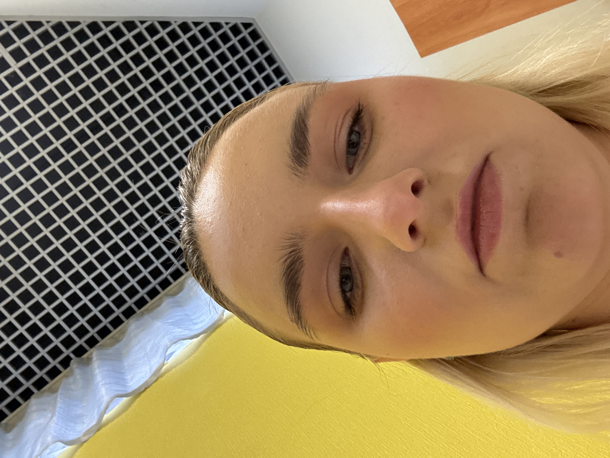 A selfie shows a woman with blonde hair, fair skin, and light eyebrows. The background includes a black and white square grid, a white ruffled surface, and a yellow surface. The photo does not provide enough information to confirm that the image was taken in St. Petersburg, Russia.