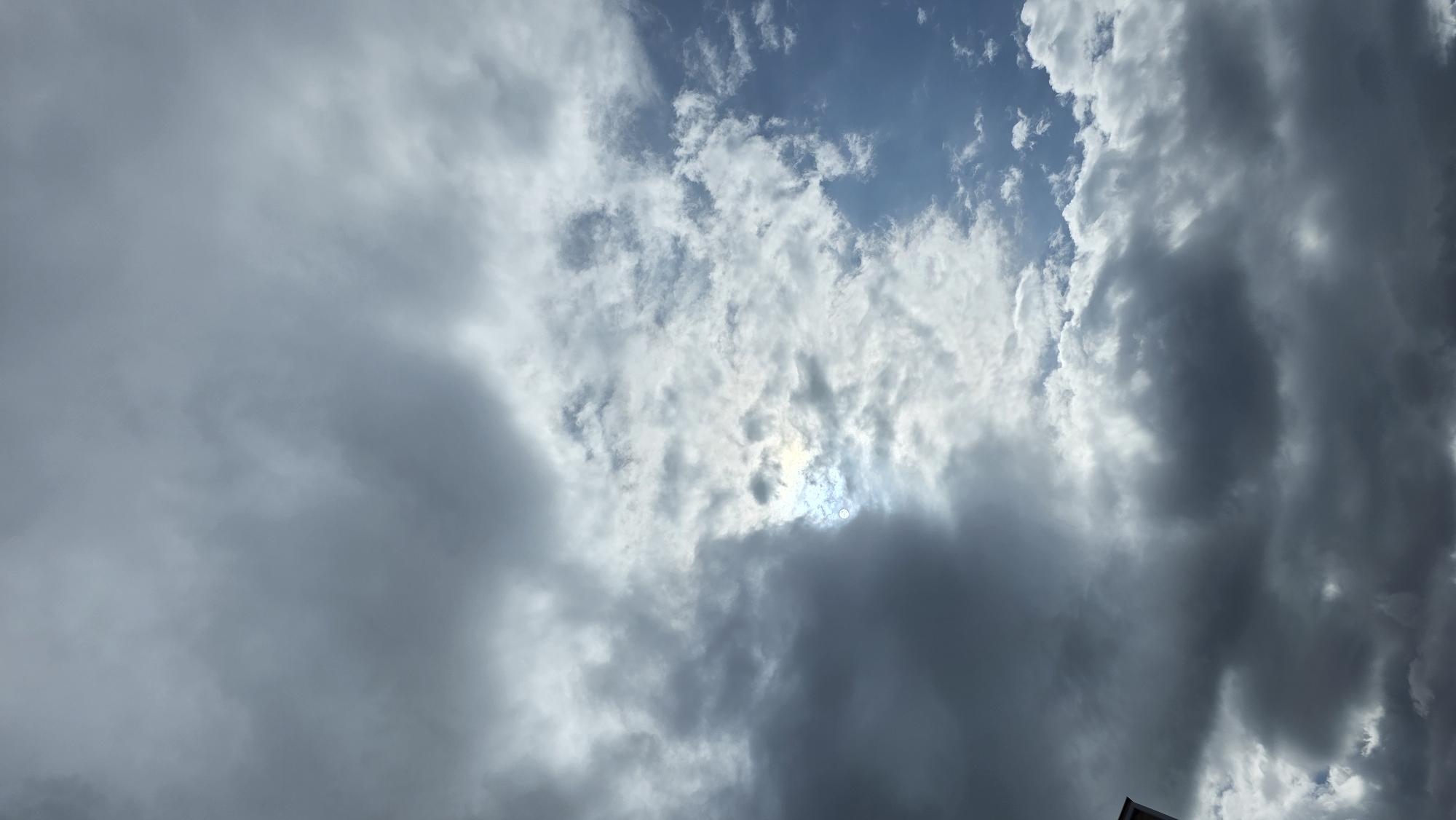 The image is a low-angle shot of a cloudy sky, with some patches of blue visible. The clouds vary in density, from thin and wispy to thick and dark. The lighting suggests the sun is behind the clouds. The image was taken in Blagoevgrad, Bulgaria.