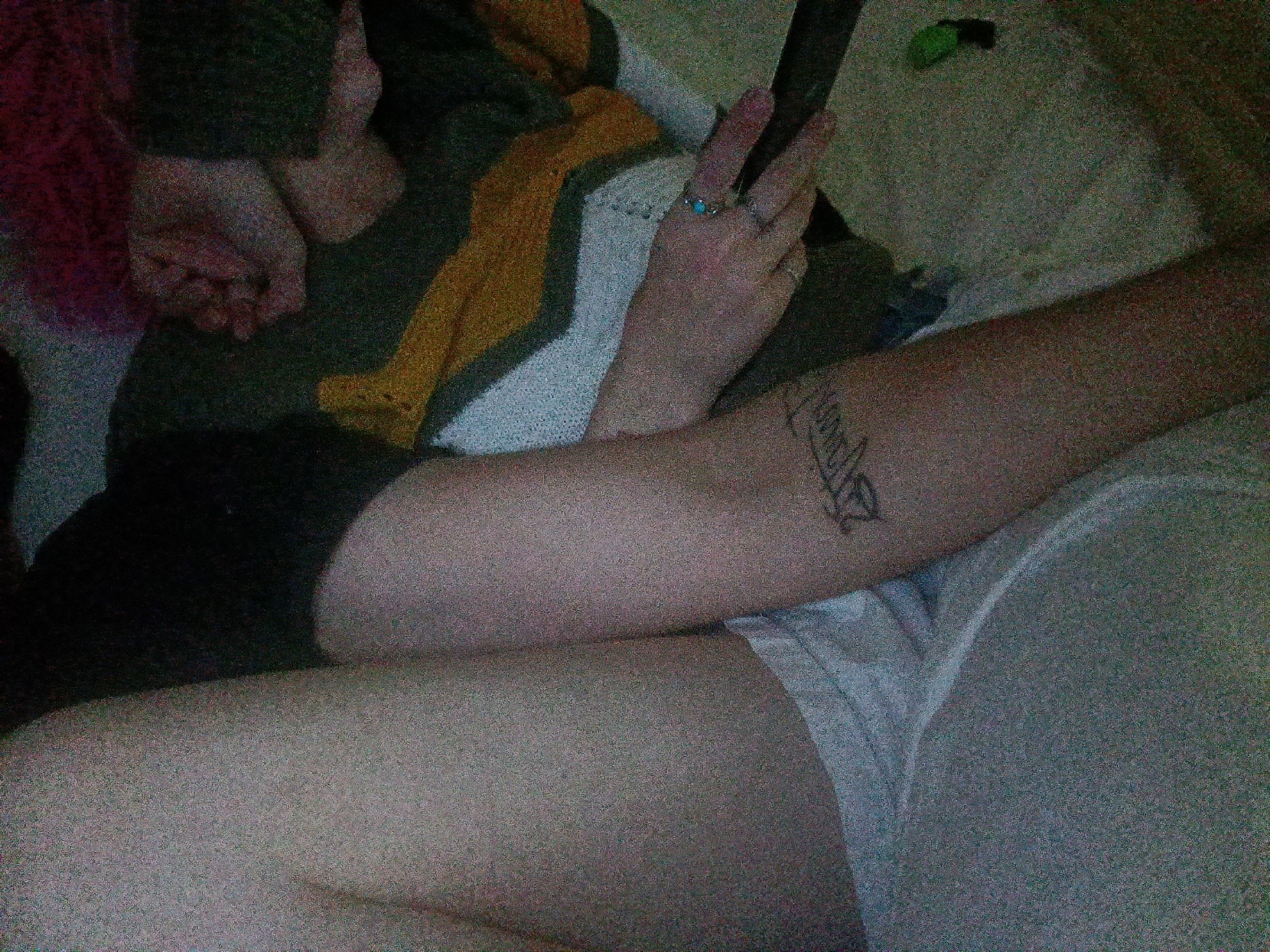 A person is lying on a gray surface, presumably a bed. The individual is wearing black shorts and white underwear. Their left arm is resting on the surface, displaying a tattoo. Their right hand is held up, showing two fingers extended in a V shape. The location in Fort Smith, United States of America, is not discernable from the image.