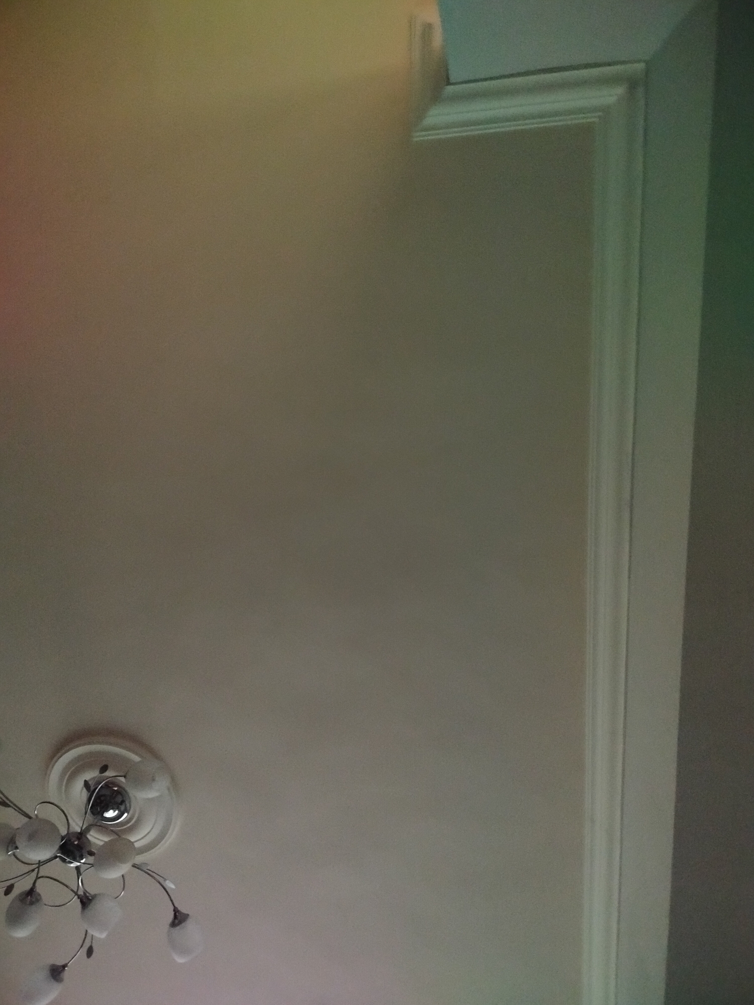 The image shows a section of a room's ceiling and upper wall. The ceiling is plain and off-white, with a circular decorative light fixture in the bottom left corner. The wall is also off-white, with a decorative white molding along the upper right edge. There is no indication of the location being Yerevan, Armenia. No people, actions, or interactions are visible.