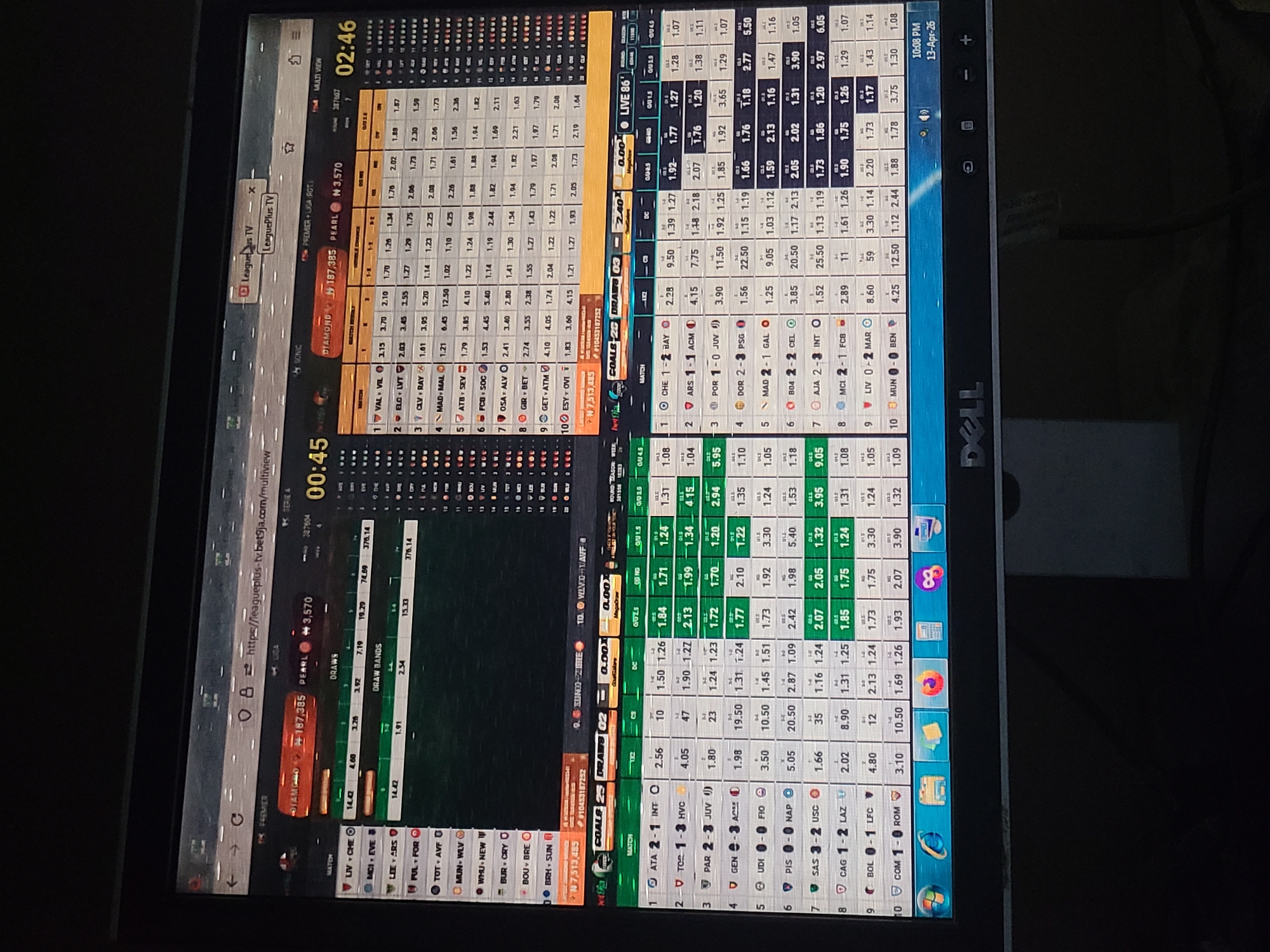 The image shows a Dell computer monitor displaying a webpage with online sports betting odds. The site, likely LeaguePlus TV (as indicated by a tab), presents odds for various soccer matches in different leagues. The interface shows a variety of data, including match details, live scores, odds for different outcomes (1X2, over/under goals, etc.), and ongoing promotions.
A smaller window at the top left displays a timer at 00:45. A similar display on the upper right corner is at 02:46. The betting interface is visually cluttered with numbers, text, and color-coded information. The photo itself appears to be taken in a dim environment, with the laptop screen illuminating the area. There are no discernible people or clues to identify a location in Jos, Nigeria. The desktop background is a nondescript gray.