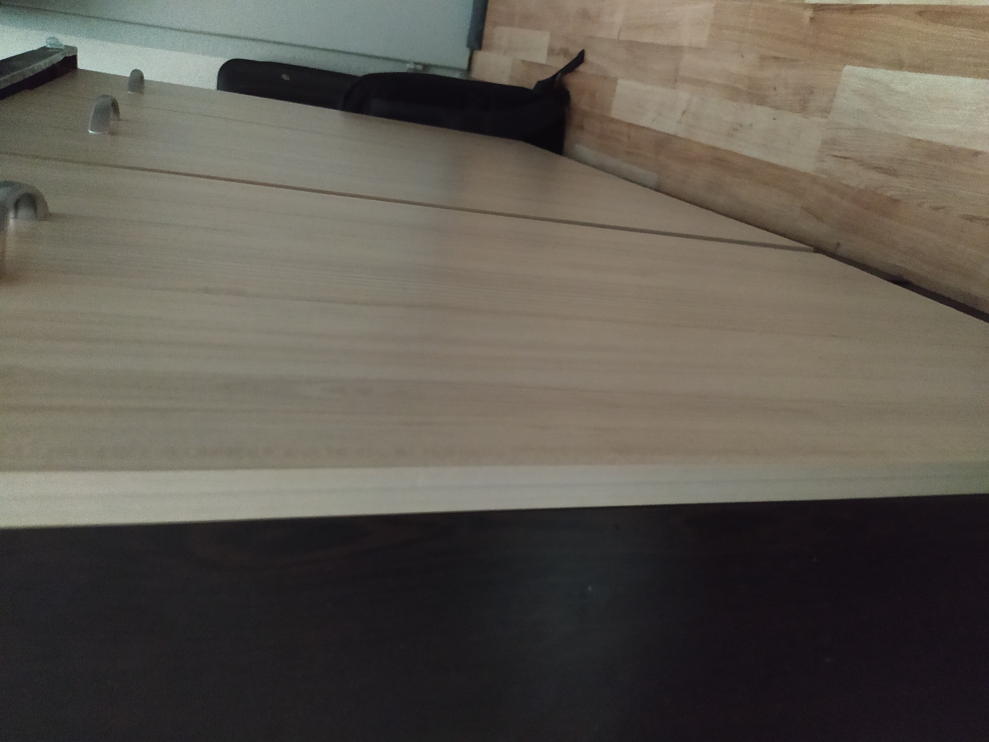The image shows a close-up, angled view of a light-colored wooden countertop with a seam running across it. Two cabinet handles are visible on the left. On the countertop, there is a black object resting near a wall. The wall is covered with horizontal wood-look panels. The bottom of the countertop is a dark brown color. The location is likely indoors. The image does not contain any information about the city of Sofia, Bulgaria.