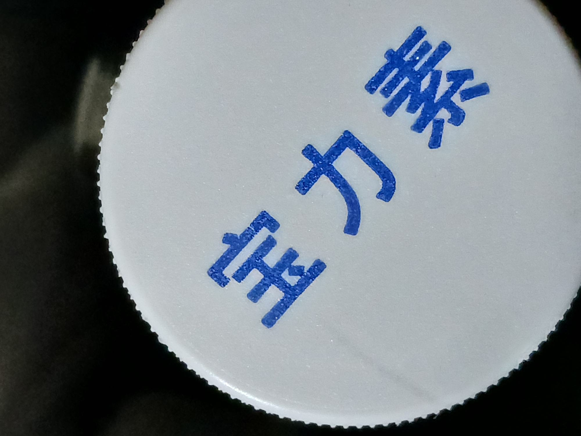 A close-up shot of a white bottle cap with blue writing on it. The writing is in Chinese characters: 活力素. The background is dark and out of focus. The edge of the cap is textured with small ridges. The image doesn't show any information regarding the location in Buenos Aires, Argentina.