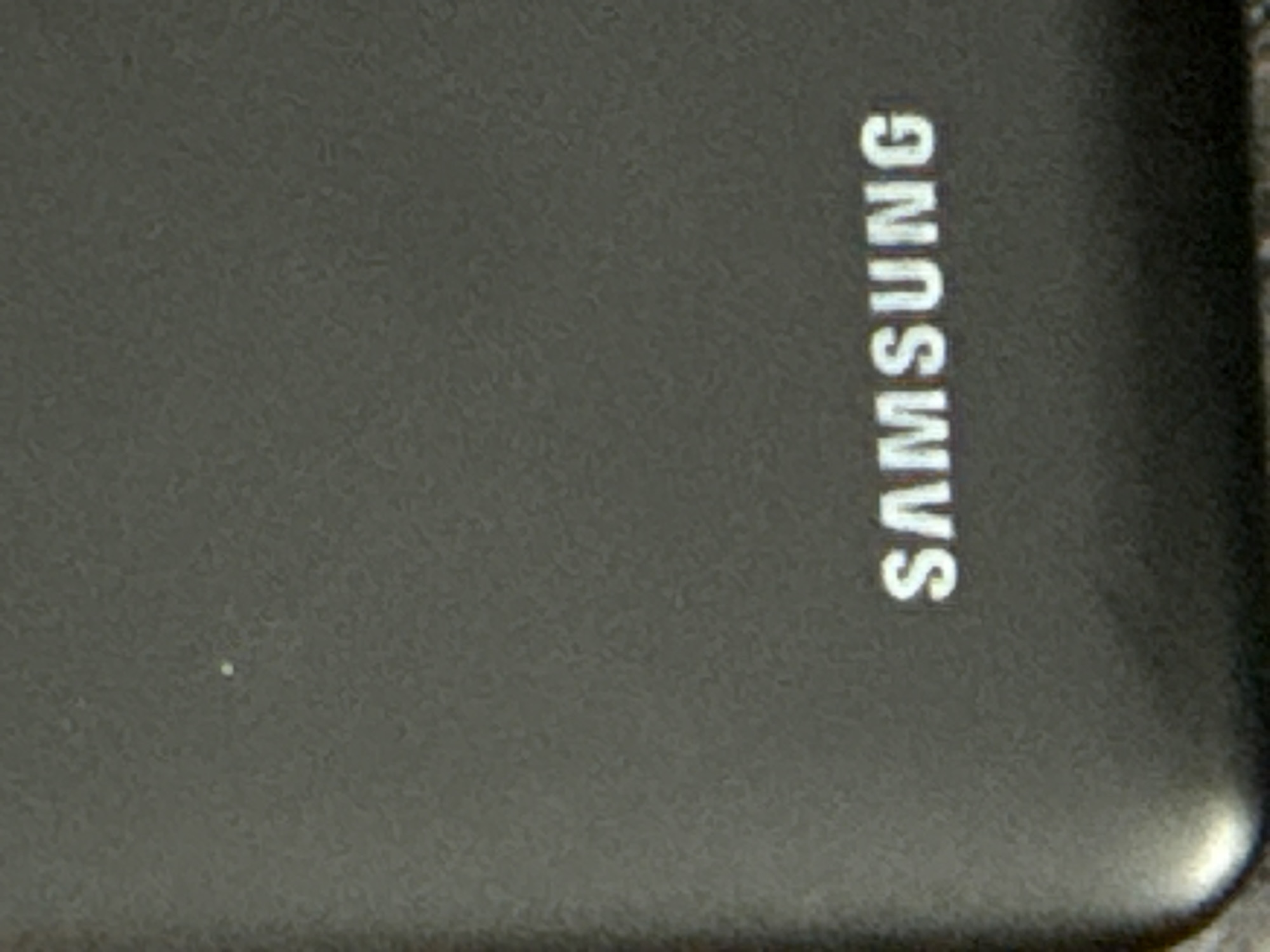 The image shows a portion of a dark-colored Samsung smartphone, with the "SAMSUNG" logo visible in white, oriented vertically. The surface appears slightly textured.