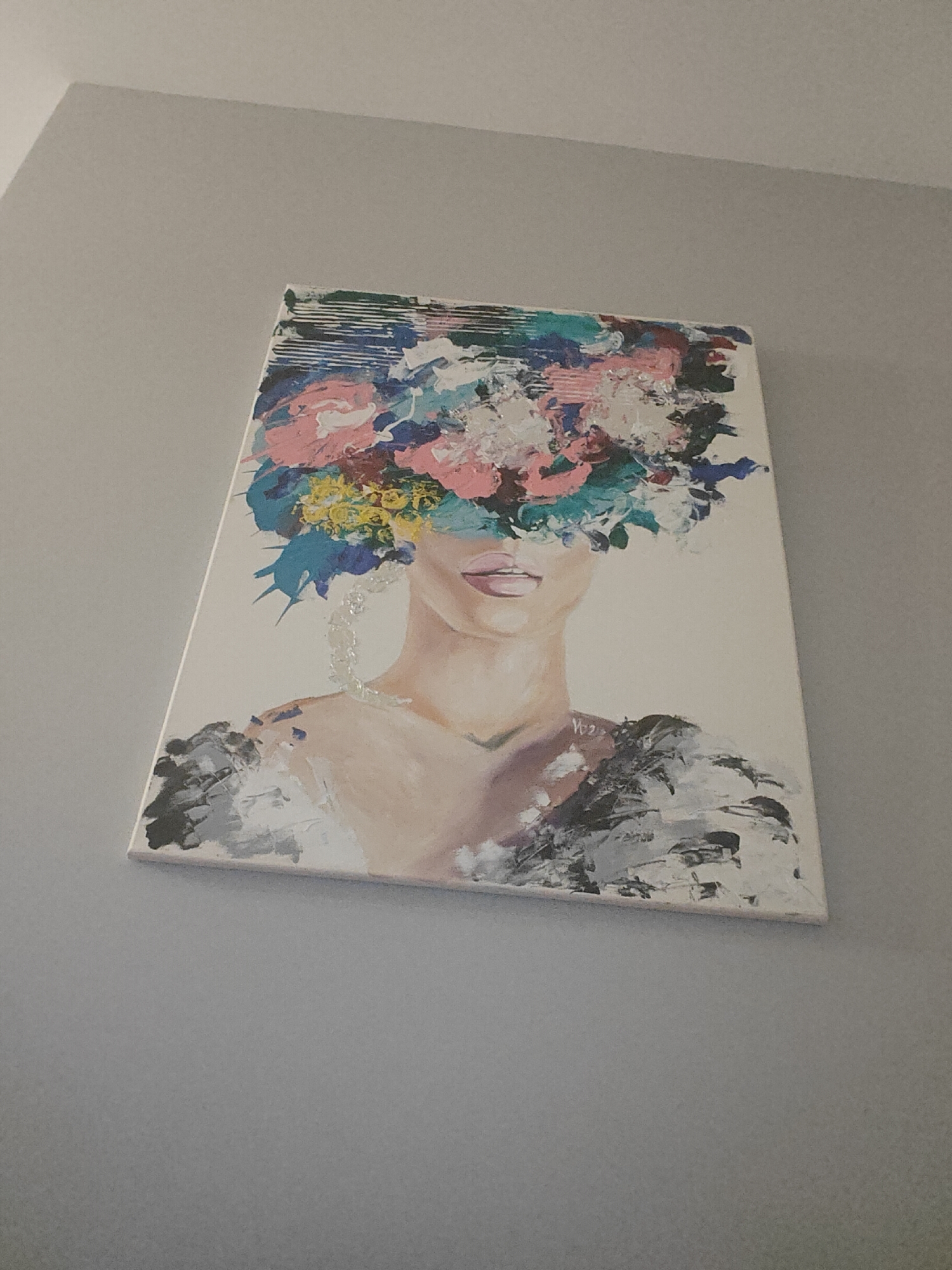 A painting of a woman with flowers covering her eyes hangs on a gray wall. The painting appears to be an impressionistic style with heavy brushstrokes and a mix of colors, including pink, blue, yellow, and white for the floral headdress. The woman's face is partially visible, with pink lips and light skin. Her shoulders are adorned with gray and black strokes, suggesting clothing or a shawl. There is no indication of the city of Sofia, Bulgaria in the image.