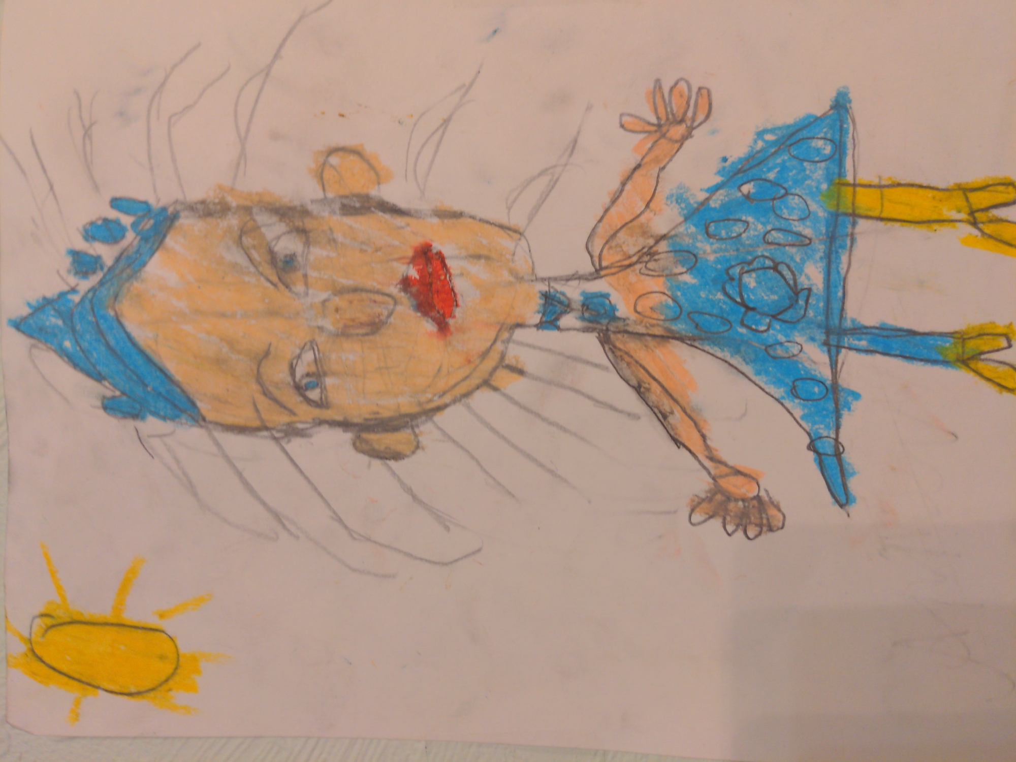 The image depicts a child's crayon drawing of a person. The person has a yellow-orange face with blue hair, a red mouth, and blue eyes. The person is wearing a blue dress with circular patterns and yellow arms. The drawing includes a yellow sun in the bottom left corner. There is no indication that the location is in Moscow, Russia.