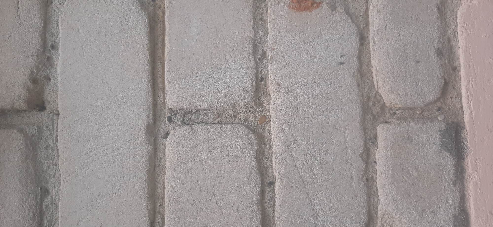 The image shows a close-up of a brick wall. The bricks are light gray and appear to be weathered. The mortar between the bricks is a darker gray. The wall has a textured surface. There is a faint pinkish hue at the bottom of the image, suggesting the presence of another painted surface or the base of the wall. The overall impression is of an outdoor environment. There are no people or discernible actions in the image. The location in Yessentukskaya, Russia is not visually evident from the image itself.