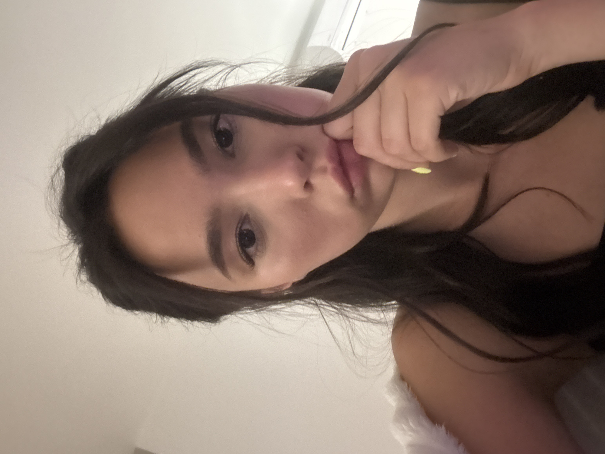 A close-up shot of a young woman with dark hair, touching her face. The location appears to be indoors, possibly a home or private residence. Her nails are painted a light yellow color. She has a serious expression on her face. The exact location in the city of Unknown, Unknown cannot be determined from the image.