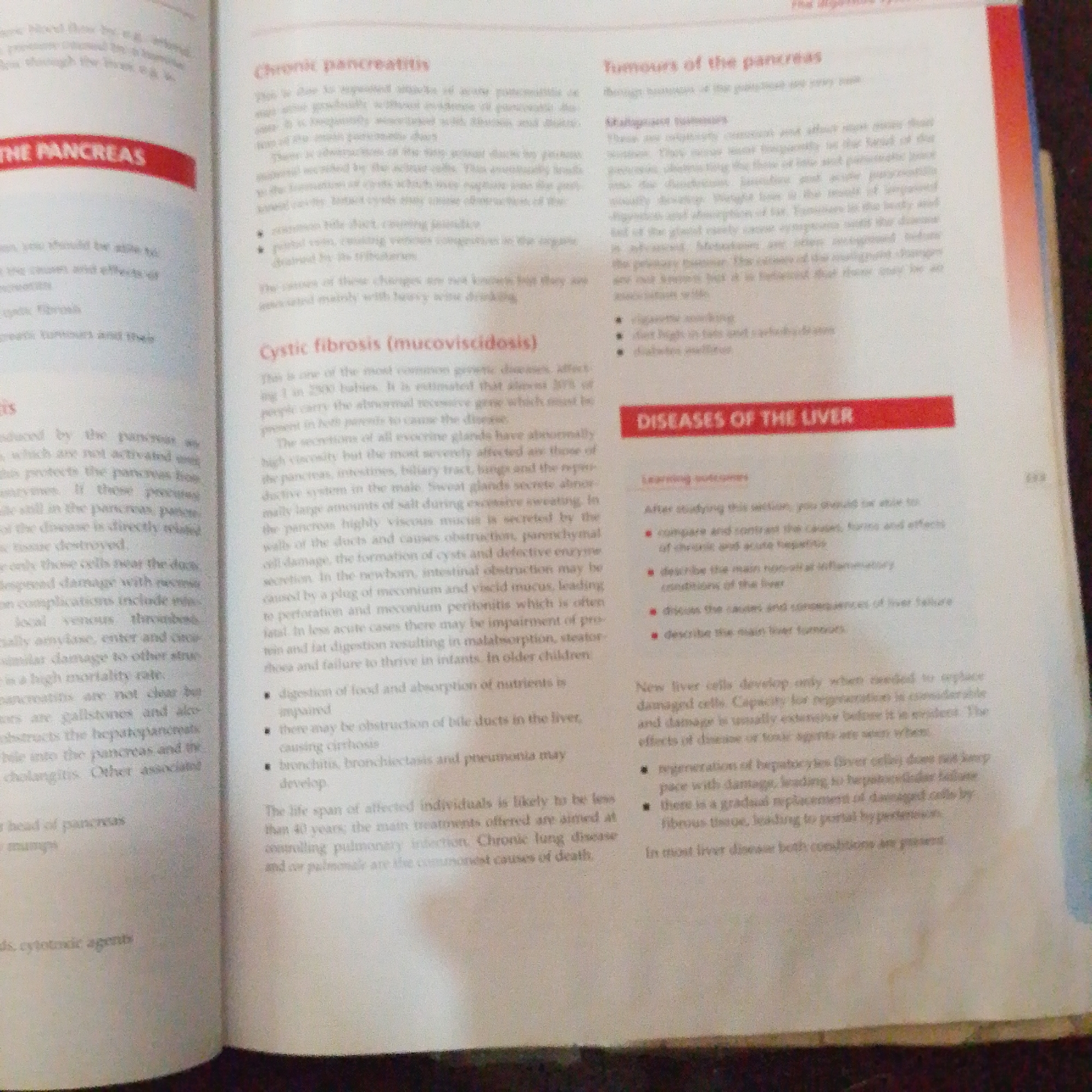 The media file is a close-up, overhead shot of an open book. The book is positioned on a flat surface, likely a table or desk, and appears to be a textbook or educational material given the presence of headings, subheadings, and bullet points. The pages are white with black text and some red highlighted sections serving as titles or emphasis.
The visible text discusses medical conditions related to the pancreas and liver. Specifically, headings include "THE PANCREAS," "Chronic pancreatitis," "Tumours of the pancreas," "Cystic fibrosis (mucoviscidosis)," and "DISEASES OF THE LIVER." There are also sections titled "Malignant tumours" and "Learning outcomes." The text details symptoms, causes, and treatments of these diseases. For example, under "Chronic pancreatitis," it mentions causes such as gallstones and alcohol. Under "Cystic fibrosis," it describes the genetic nature of the disease and its effects on various organs. The "DISEASES OF THE LIVER" section discusses liver cell regeneration and the effects of damage.
There are no people, objects, or specific scene details beyond the book itself. The lighting suggests an indoor setting, likely during the daytime due to the brightness of the page. There are no discernible emotions conveyed. The image is purely informative, focusing on the textual content of the book. The location context of Jalingo, Nigeria is not visually indicated within the image itself.